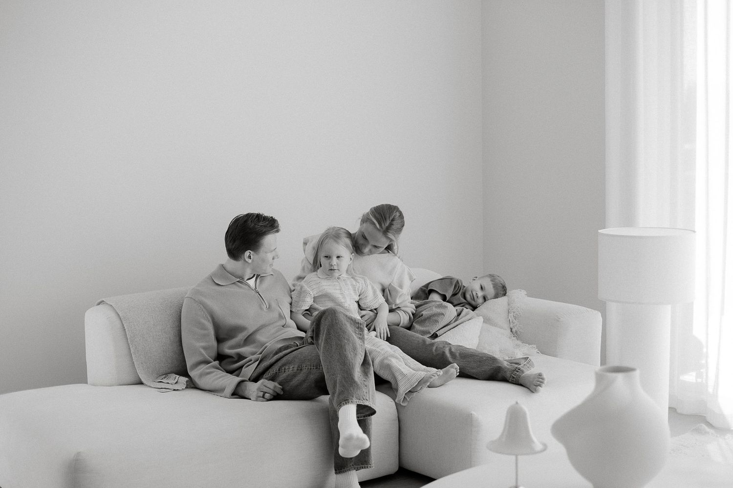 Black and white photo of three children relaxing together on a white sofa in a bright, minimalist living room.