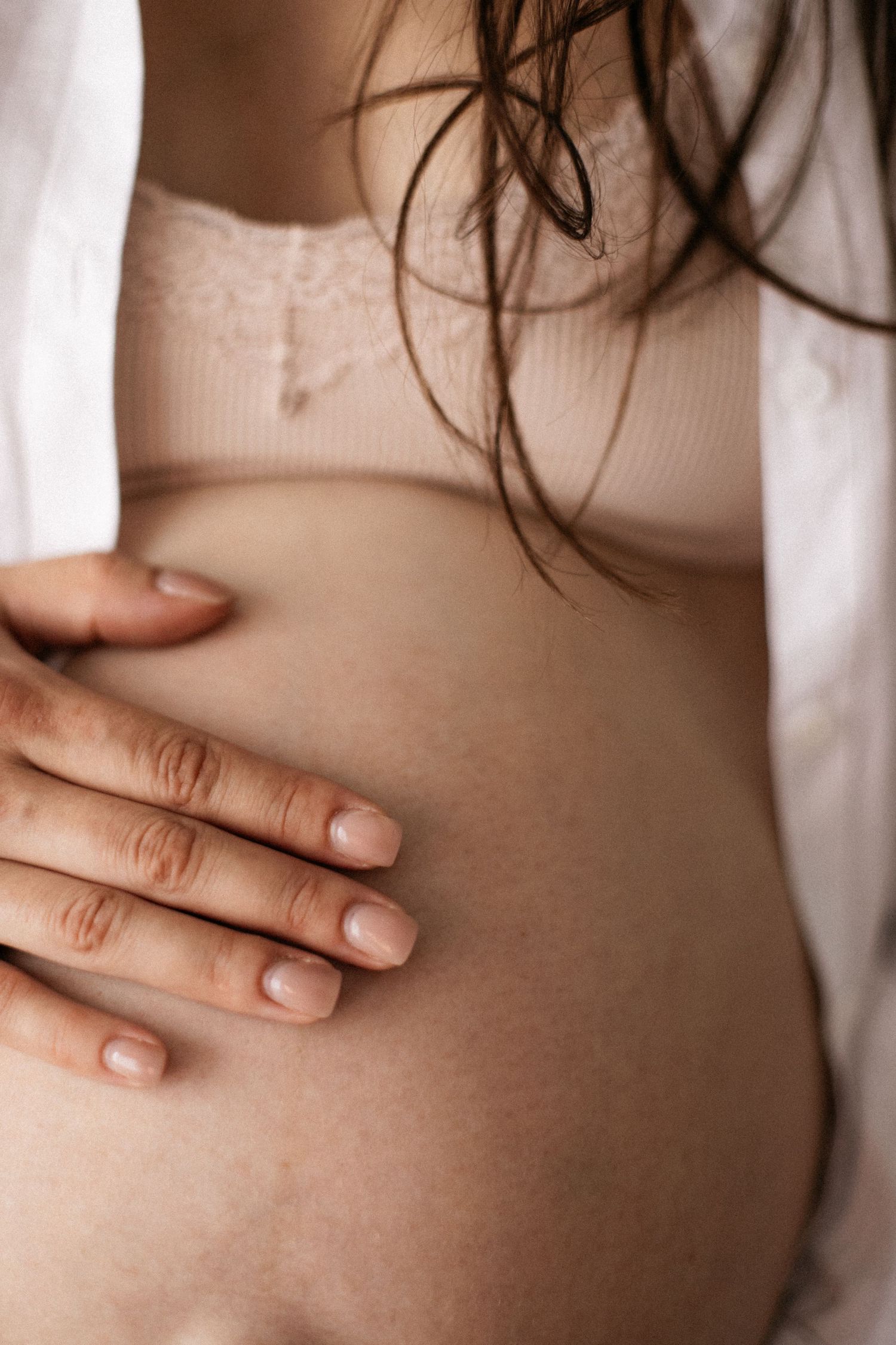 Close-up of a pregnant woman gently cradling her bare baby bump with one hand, wearing a light pink top.
