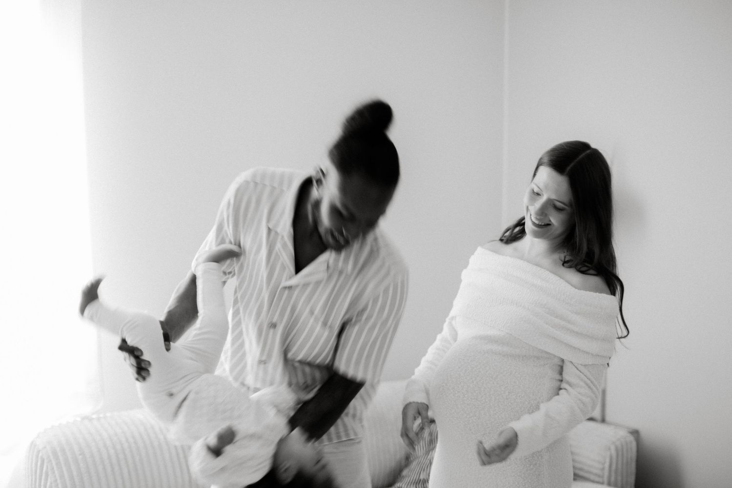 Two women having a fun pillow fight in black and white photography, wearing pajamas against a white wall.