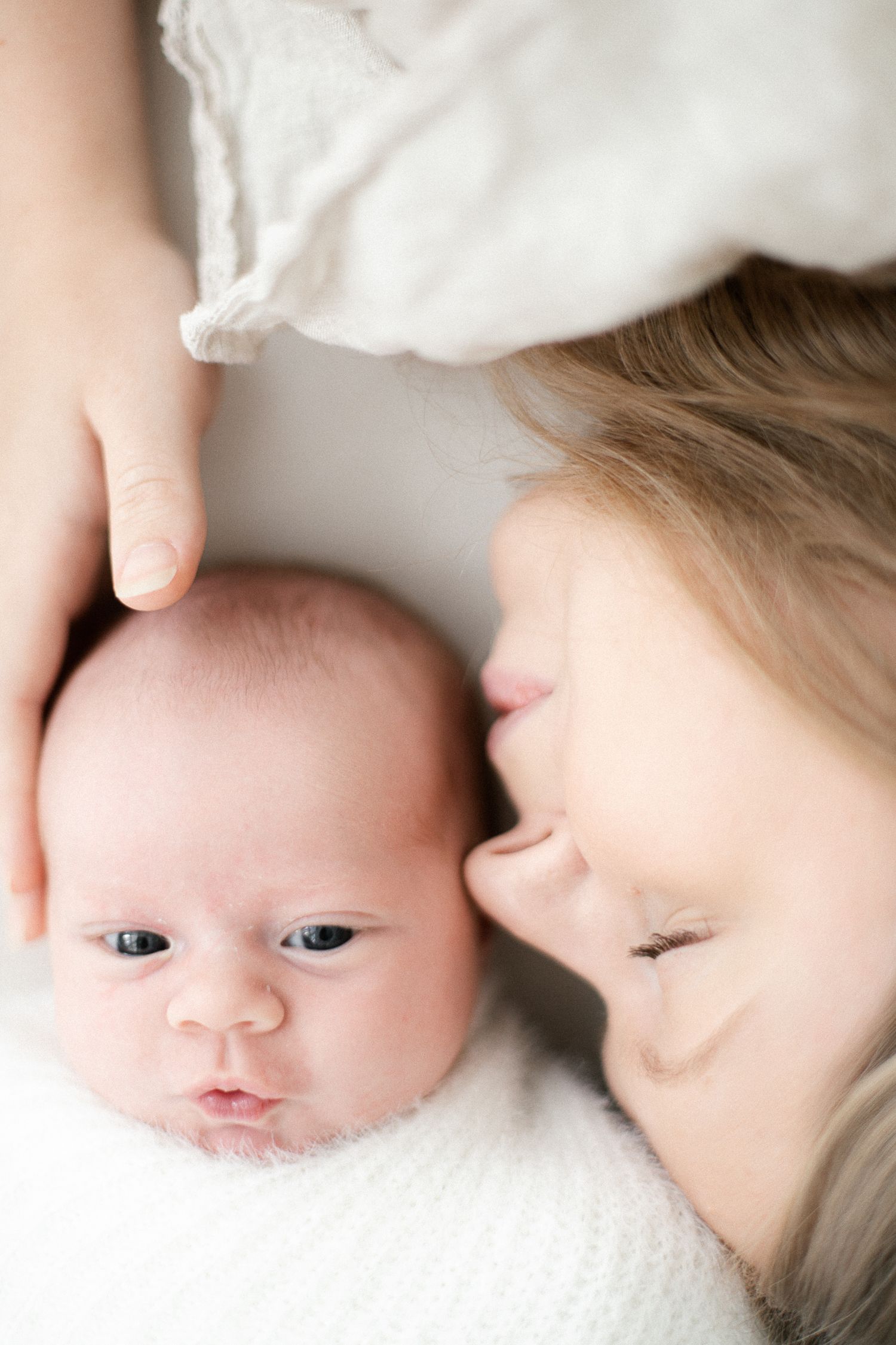 A tender moment of a mother lying beside her newborn baby, gently cradling the infant's head on a white blanket.