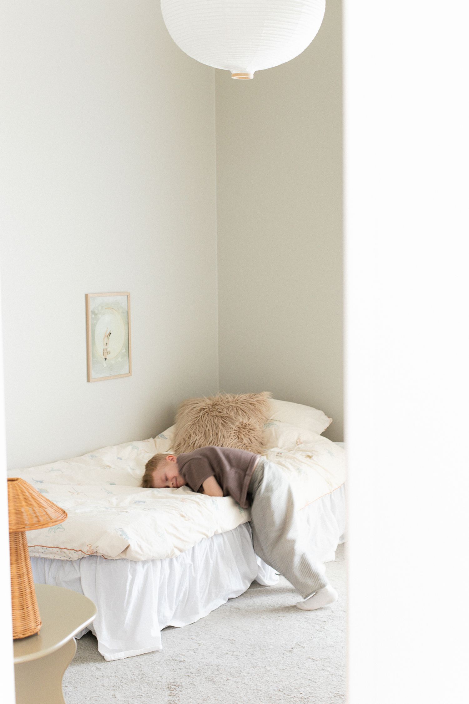 Child sleeping face-down on a white bed with linen pillows in a minimalist Scandinavian bedroom with globe pendant light.