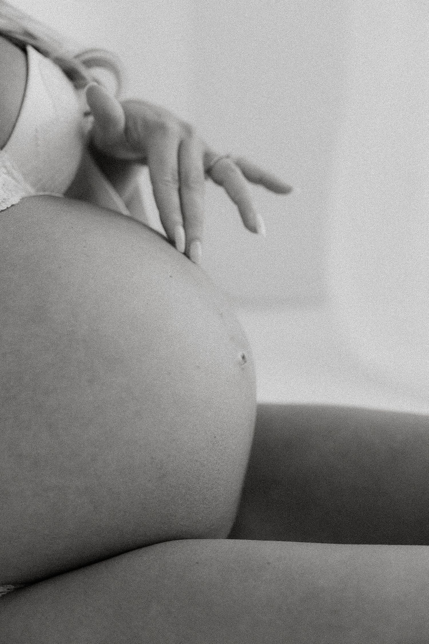Black and white close-up of a pregnant woman cradling her bare baby bump with one hand.