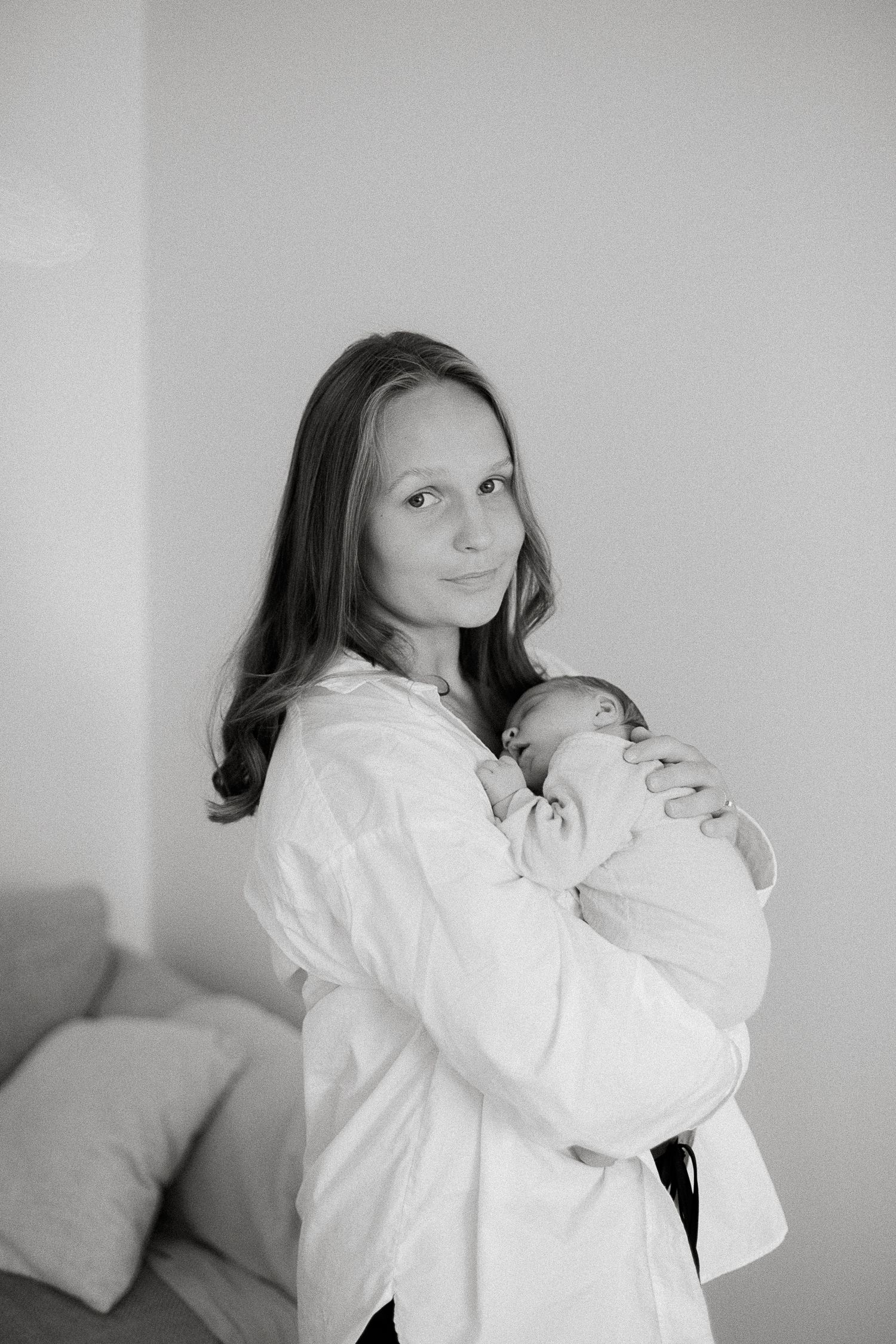Black and white photo of a young mother tenderly holding her newborn baby close to her chest indoors.