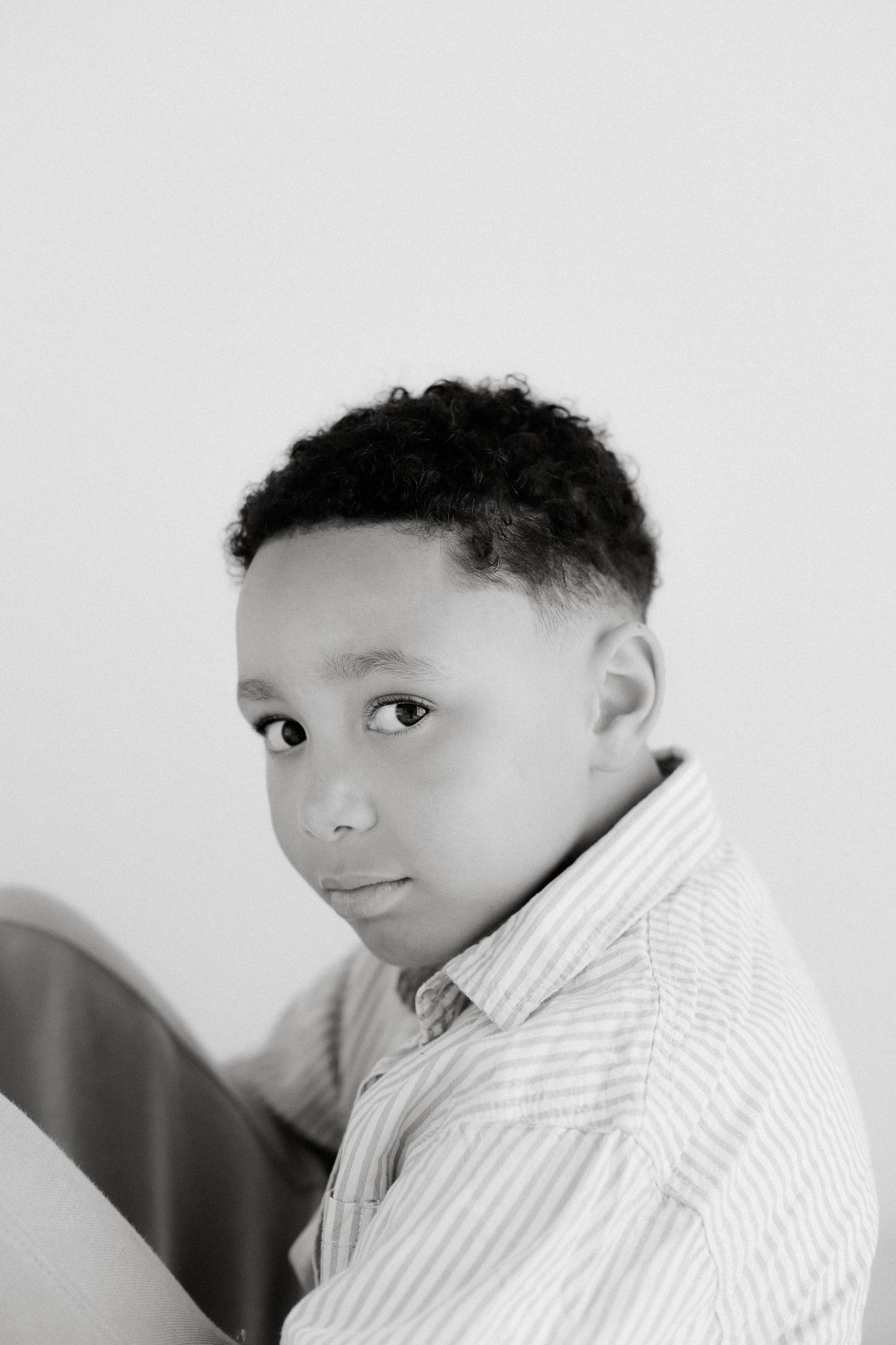 Black and white portrait of a young African American boy in a striped shirt looking at camera.