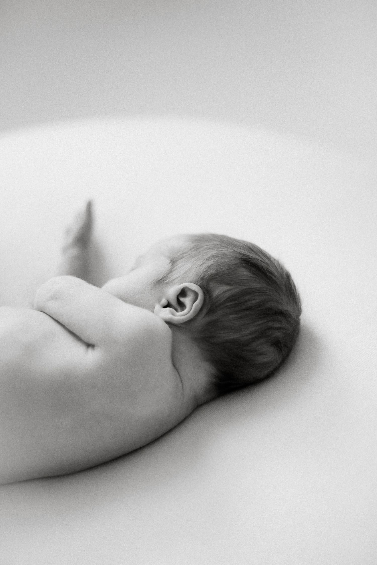 Black and white photo of a newborn baby lying on its side, showing delicate ear and soft skin details.