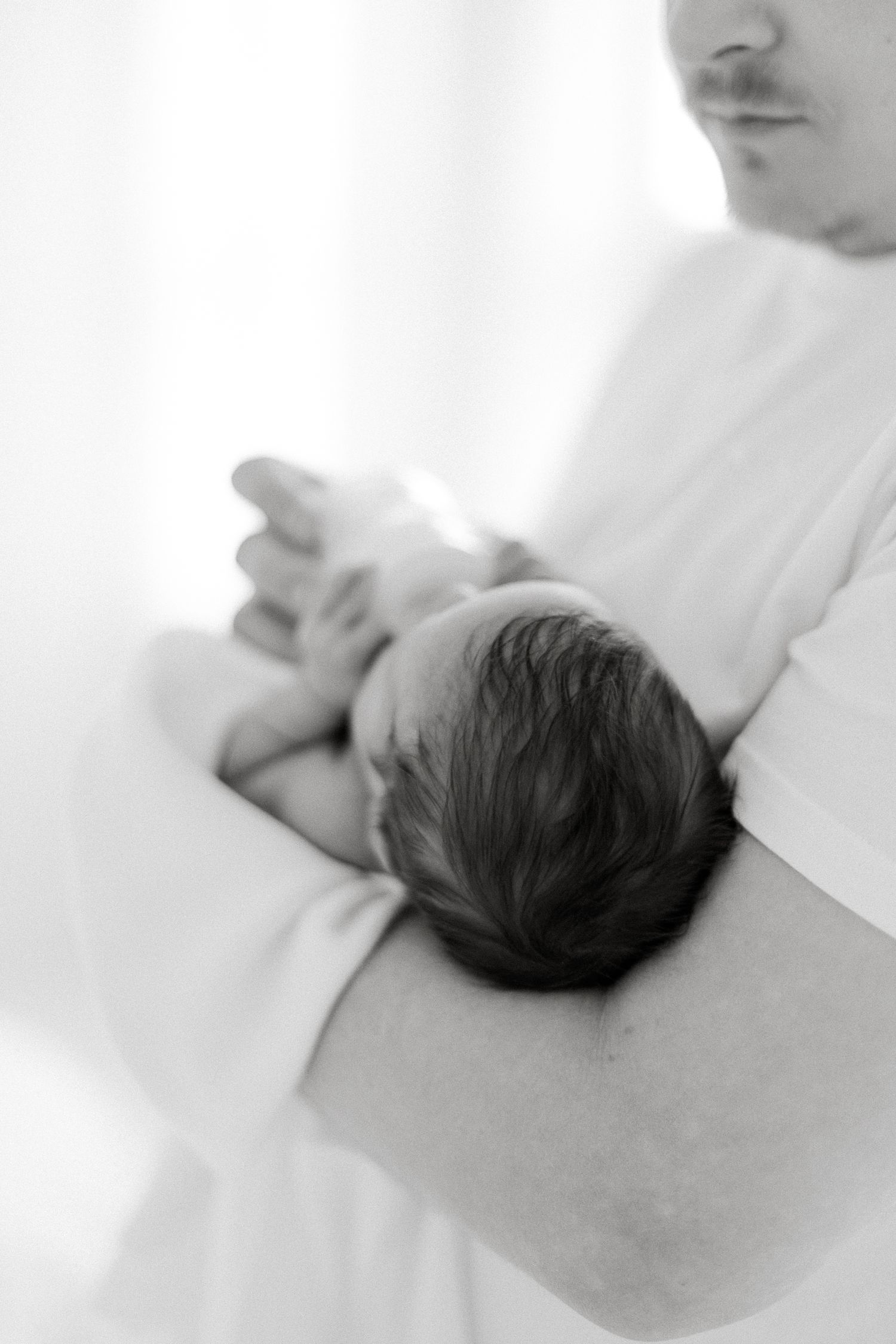 Black and white photo of parent holding newborn baby with tiny feet visible, capturing intimate bonding moment.