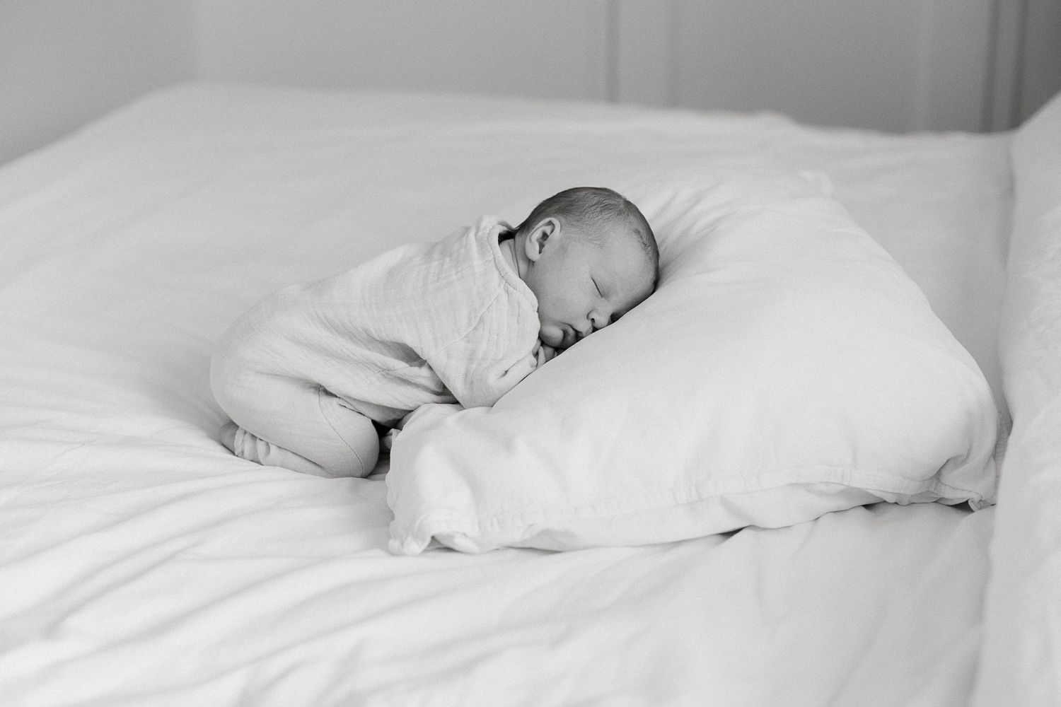 Newborn baby sleeping peacefully on white pillow wrapped in soft blanket, black and white photography.
