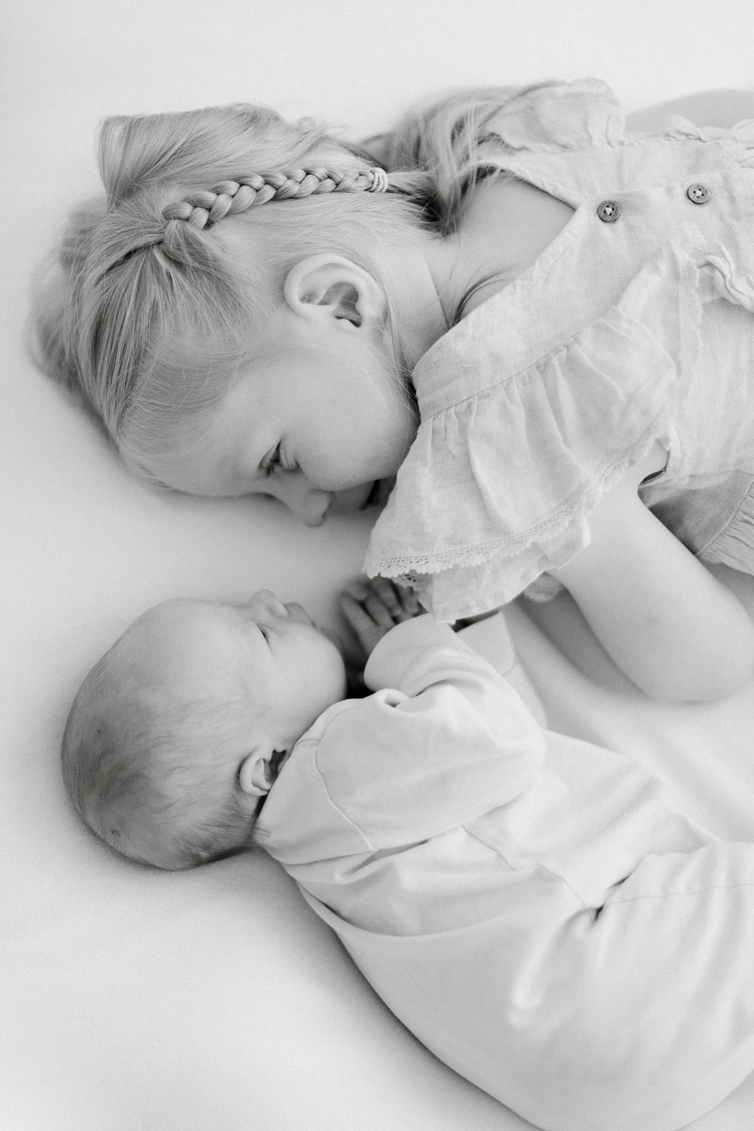 Black and white photo of a young girl with braids tenderly looking at her newborn sibling lying beside her.
