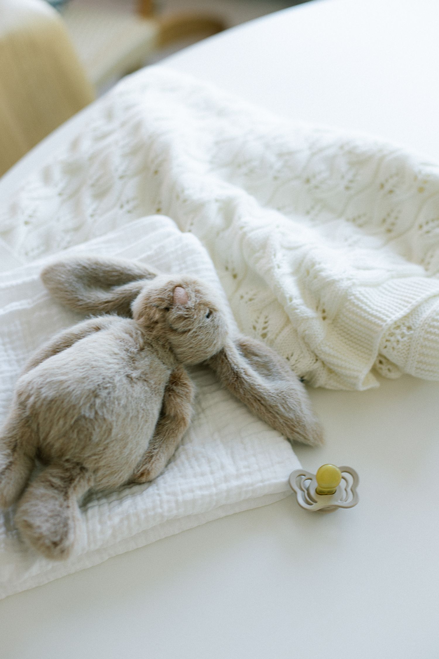 Soft grey bunny toy with pacifier on white muslin cloth and knit blanket, perfect for newborn baby essentials.
