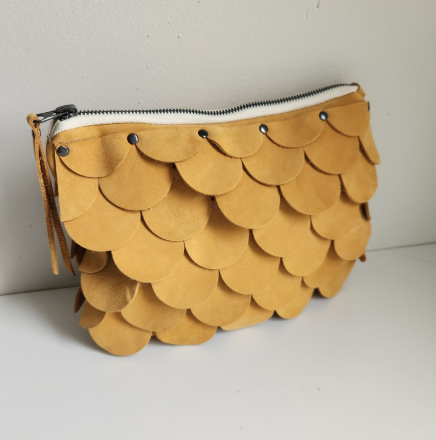 Mustard yellow leather clutch purse with decorative scalloped fish scale pattern and silver zipper closure.