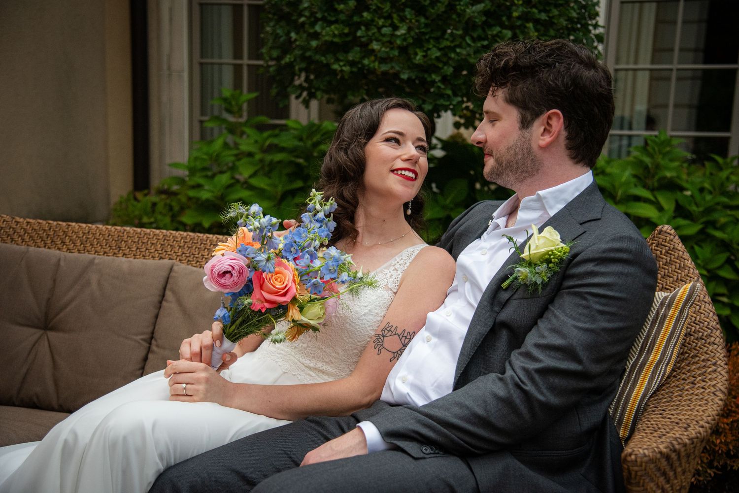 Couple shares intimate moment on outdoor patio with wicker furniture and greenery.