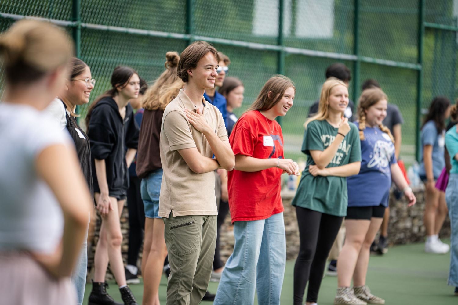 Line of spectators watching from behind a fence at an outdoor sporting event.