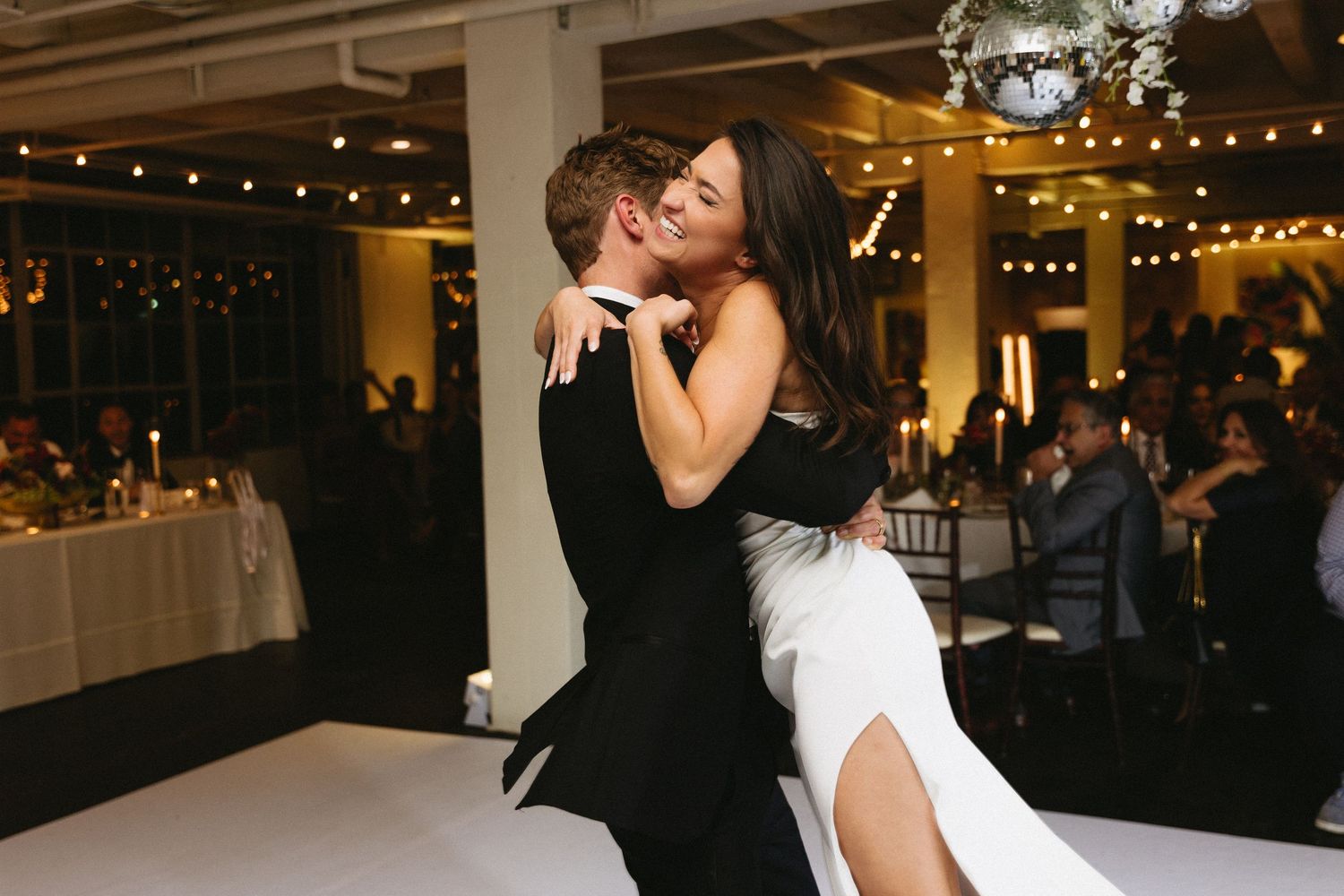 Bride and groom share romantic first dance embrace at elegant wedding reception with string lights.