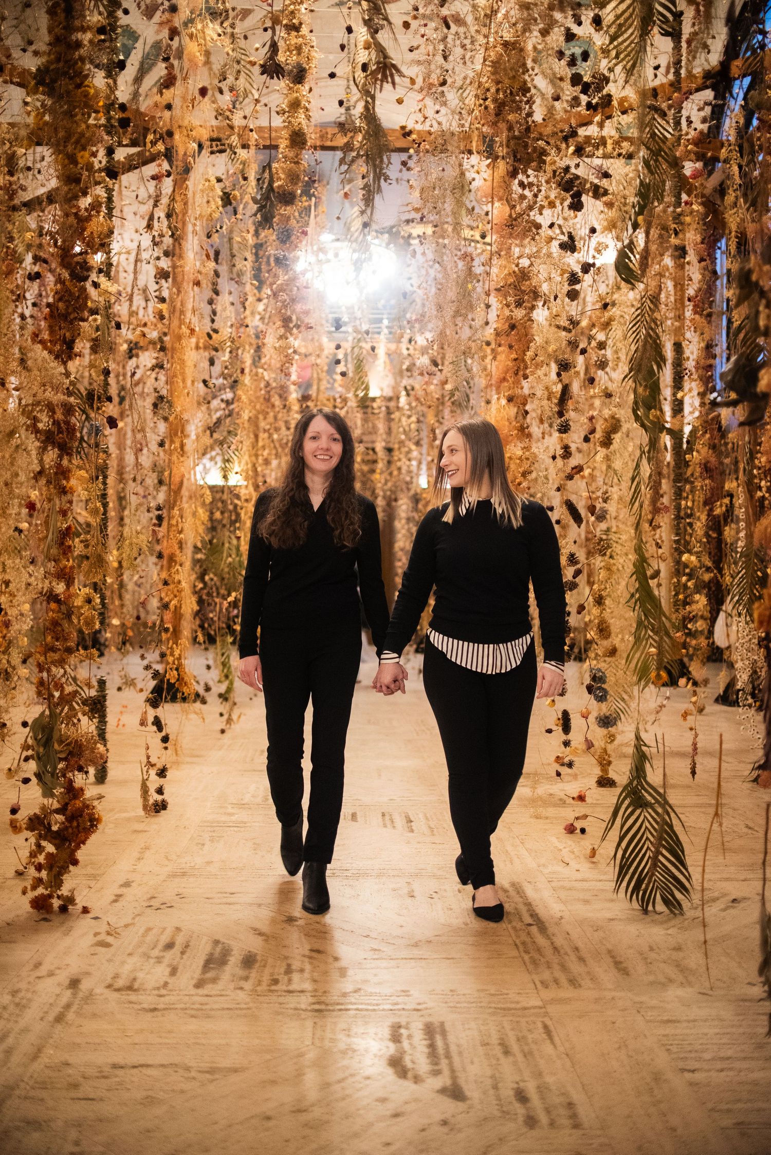 Couple walking hand in hand through a magical corridor with hanging golden decorations and twinkling lights.