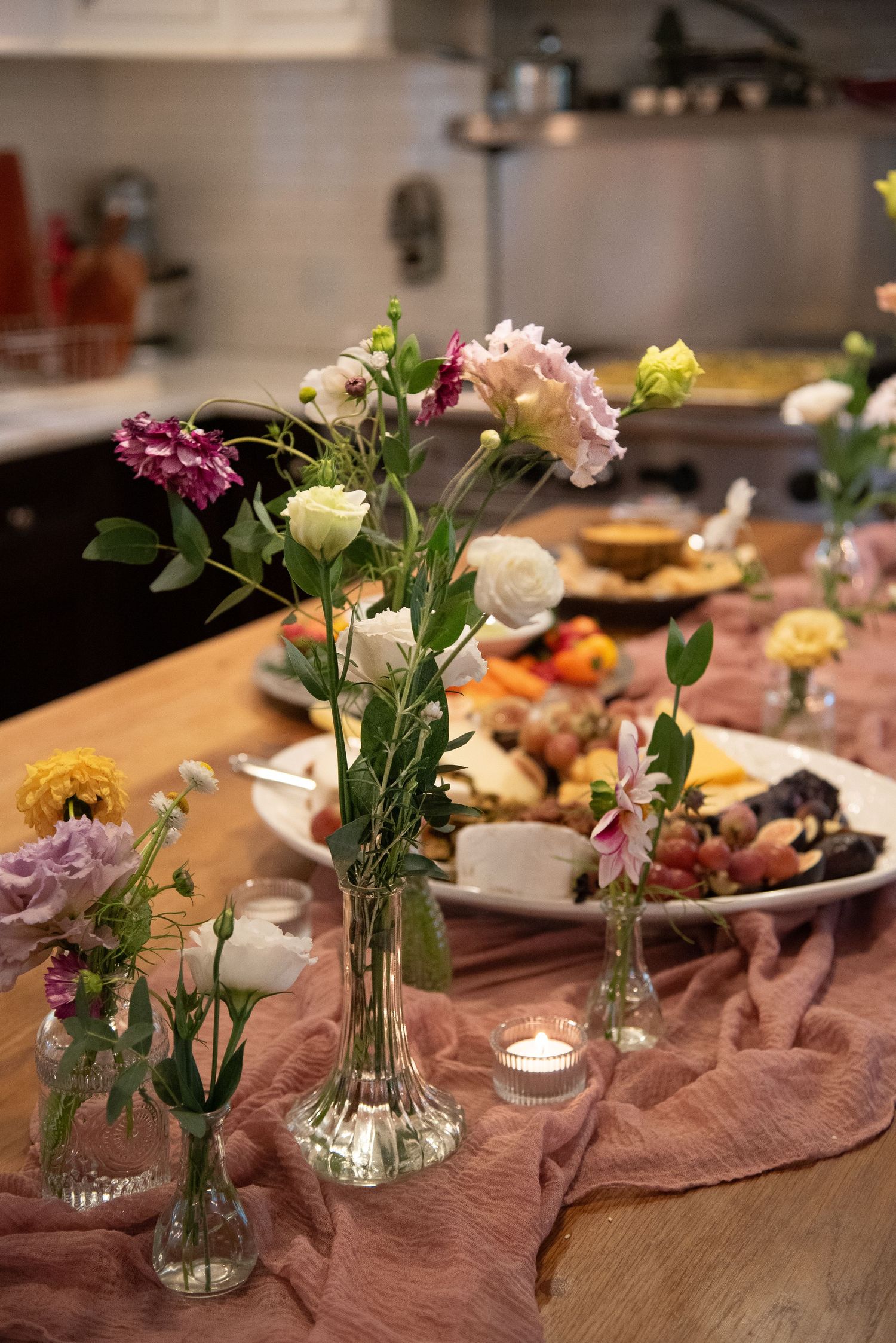 Fresh flowers in small glass vases decorating a wooden table with candles and table settings.