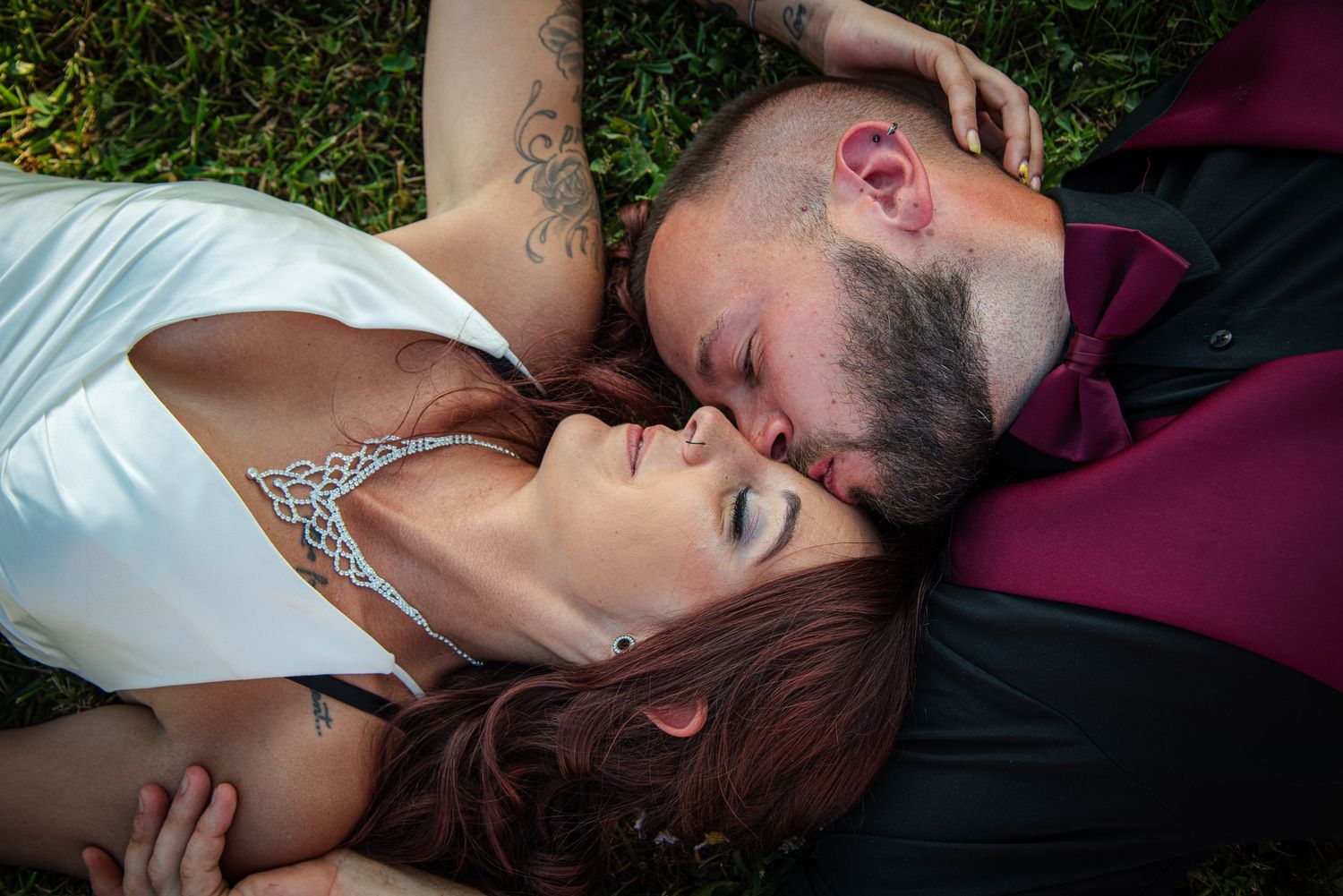 Romantic couple lying together on burgundy fabric in an intimate outdoor setting.