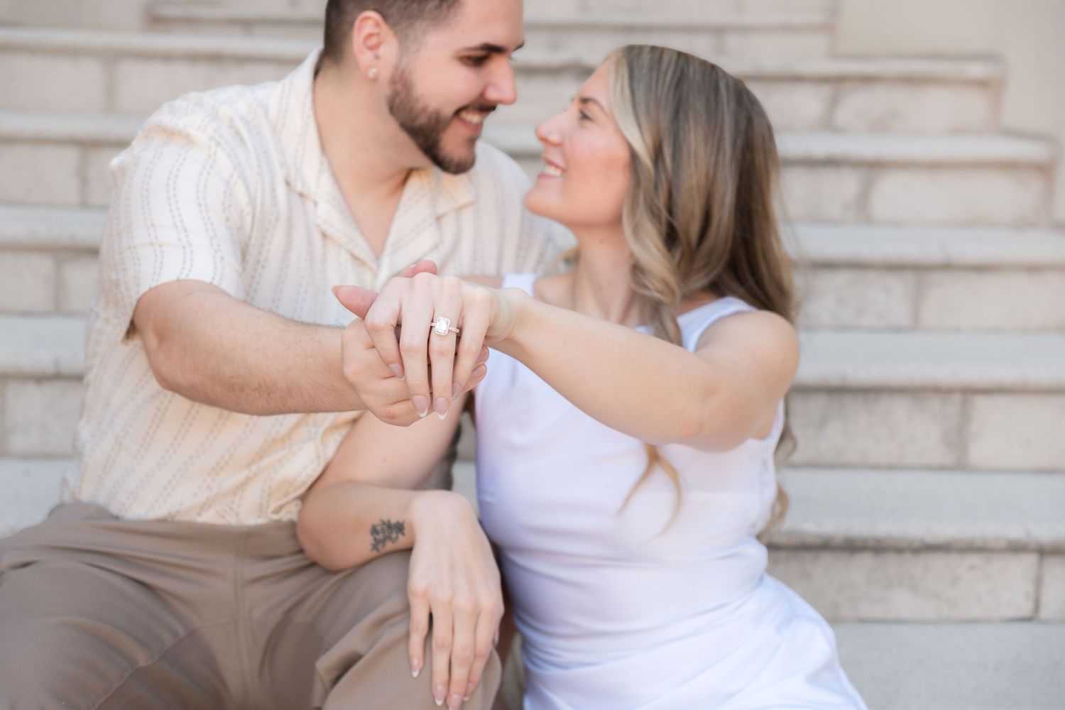 Romantic couple poses together on outdoor stone steps in matching white outfits.