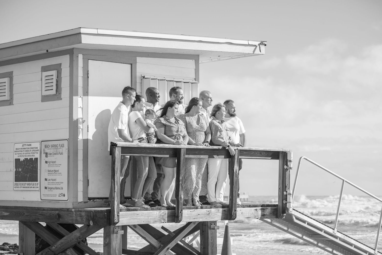 Group of people posing together on a beach lifeguard tower overlooking the ocean on a sunny day.