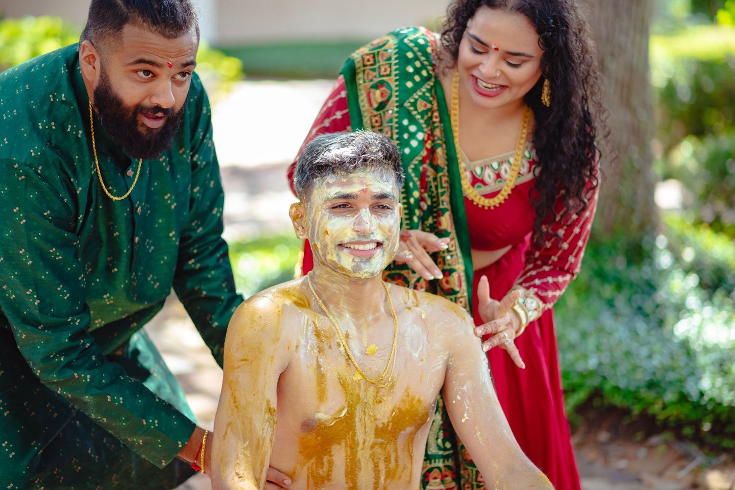 Indian wedding Haldi ceremony with turmeric paste applied to groom, surrounded by smiling family in traditional attire.