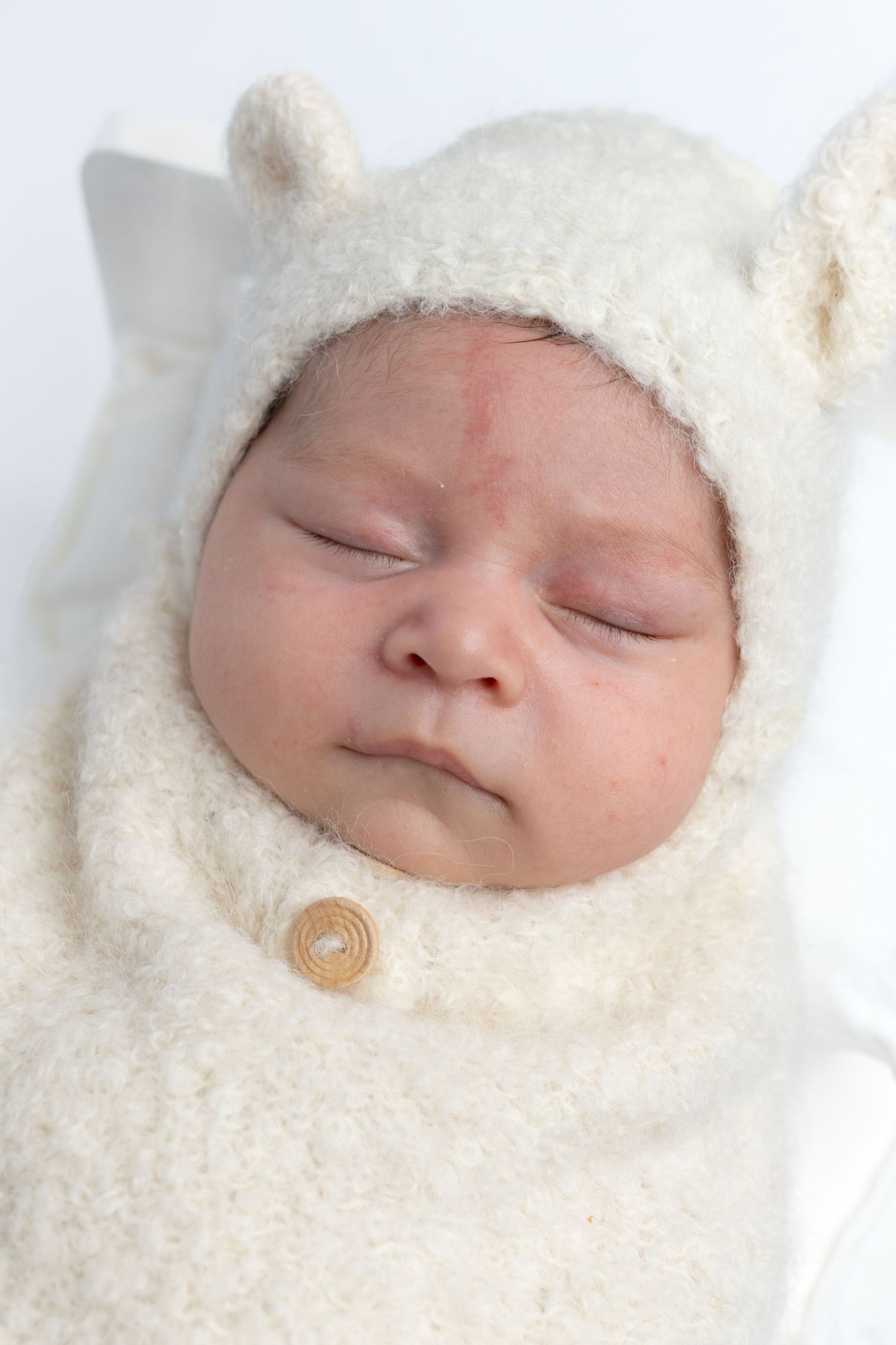 Adorable newborn baby sleeping swaddled in a cream teddy bear costume with ear hat.
