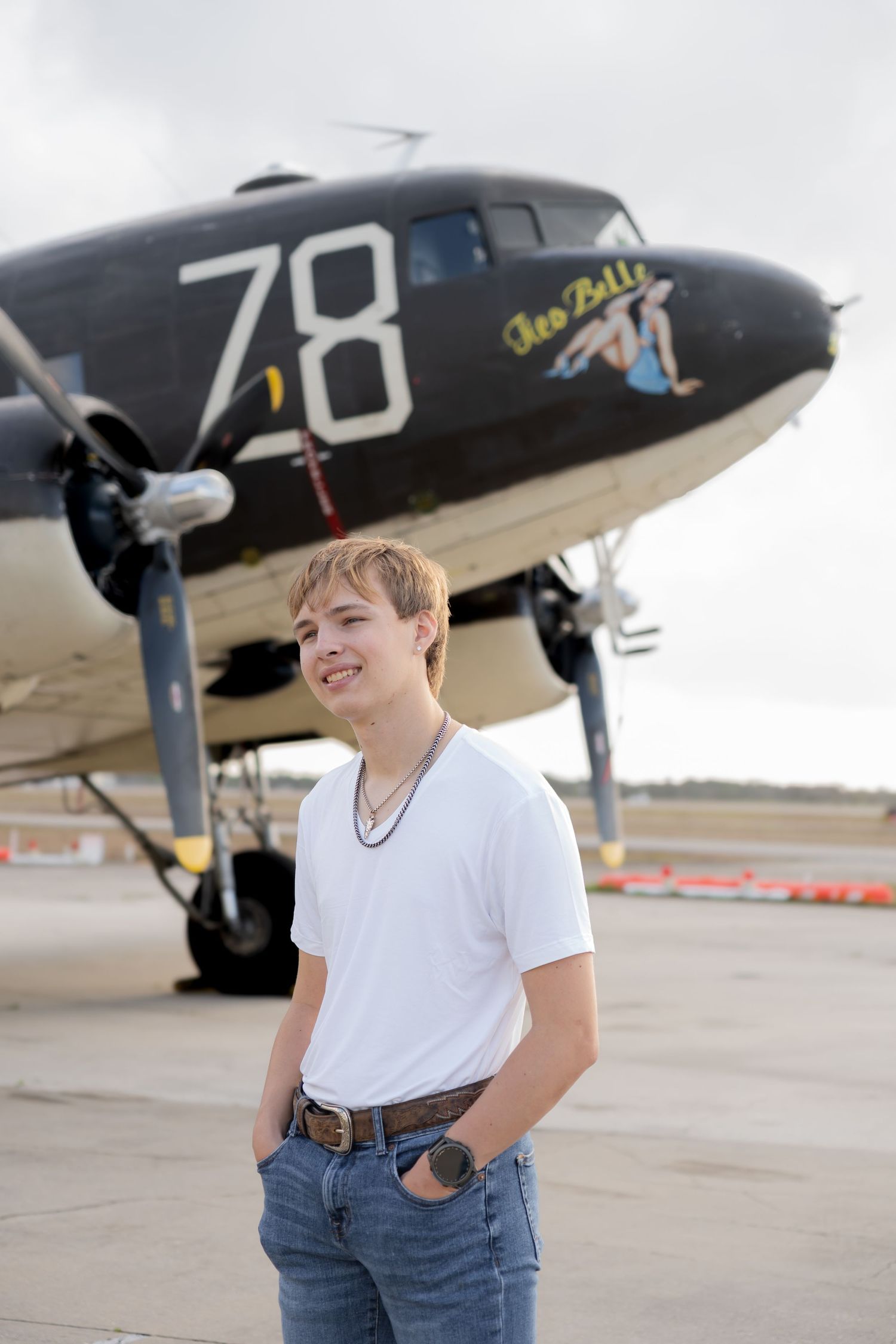 Smiling teen boy in white t-shirt standing in front of vintage WWII aircraft numbered 78.