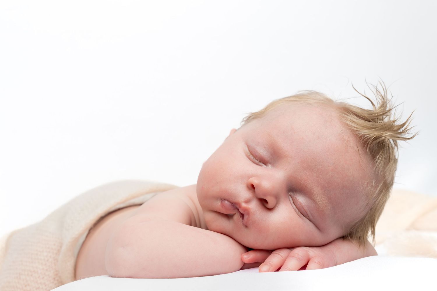 Peaceful newborn baby sleeping soundly on a white surface, wrapped in a soft beige blanket.
