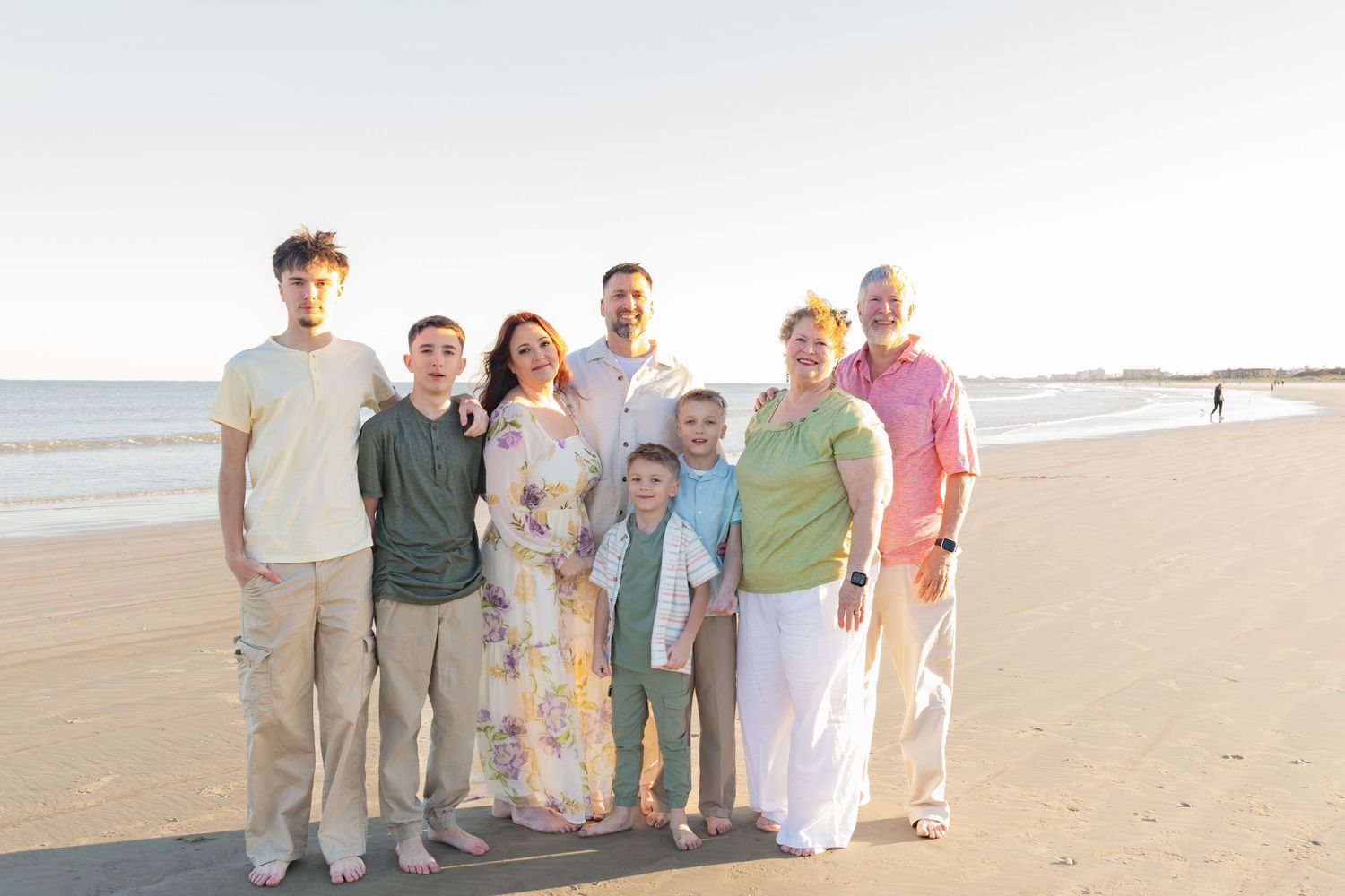 Family of eight smiling together on a sandy beach at golden hour with ocean waves in the background.