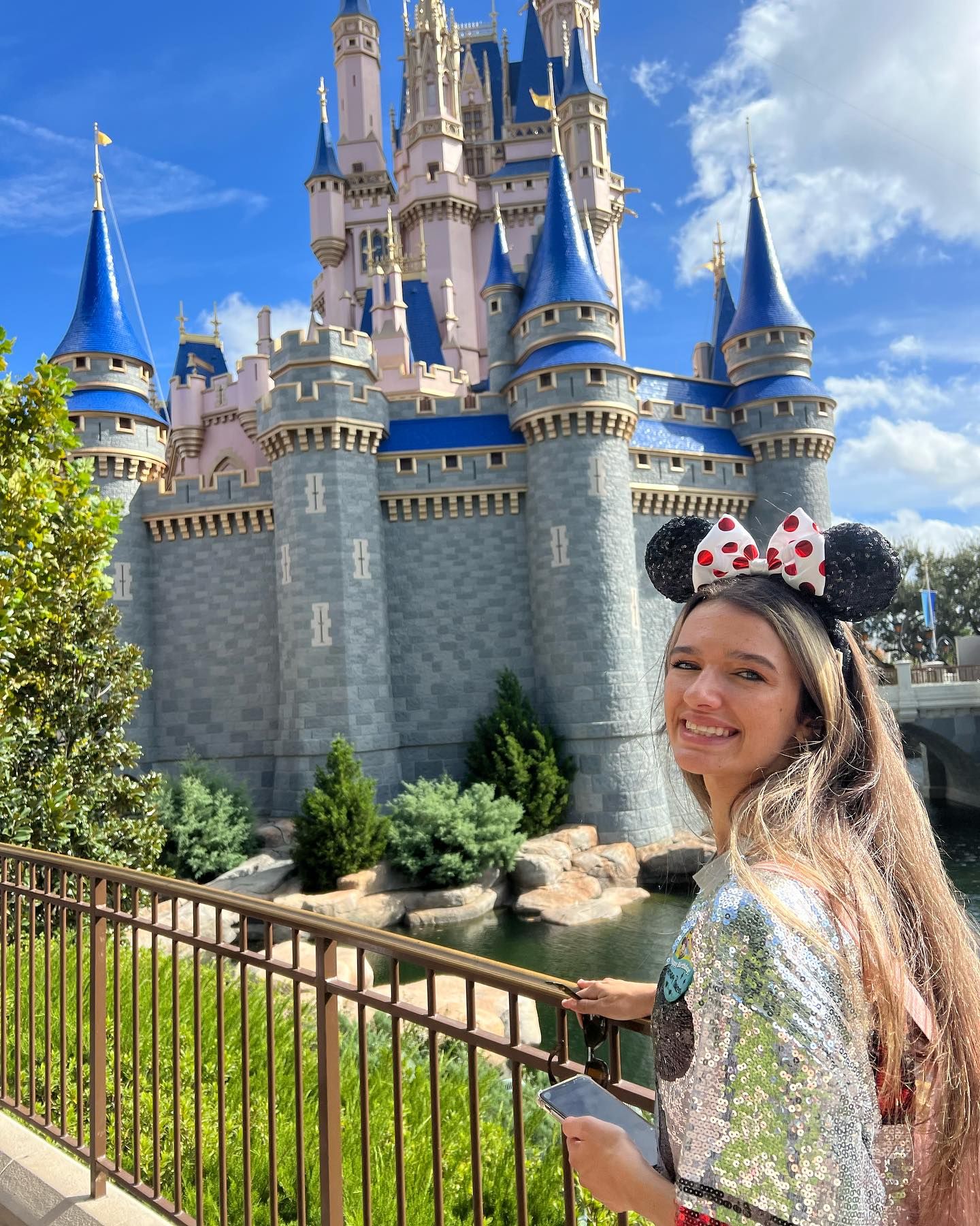 Smiling woman wearing Minnie Mouse ears posing in front of Cinderella Castle at Walt Disney World.