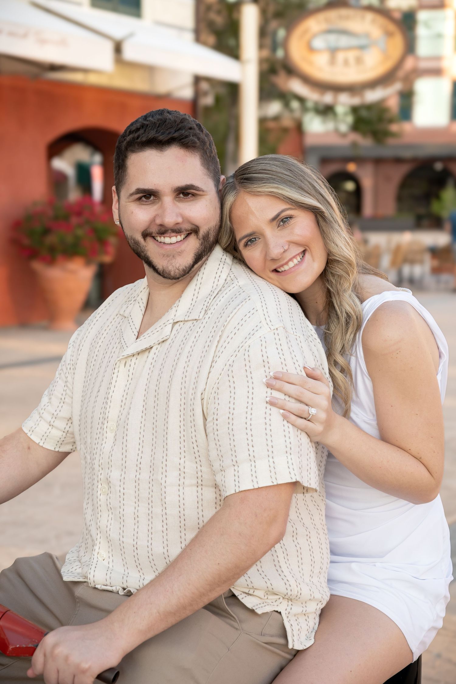 Smiling couple posing together outdoors, man in striped shirt with woman in white top leaning on him.