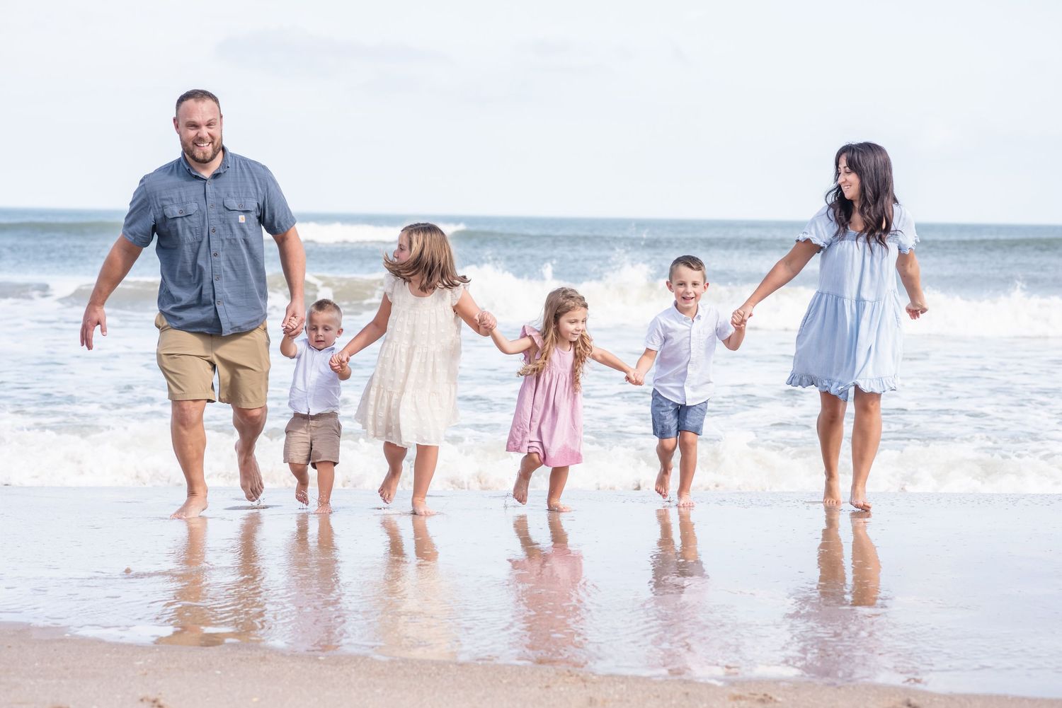 Happy family of six holding hands walking along ocean shoreline.