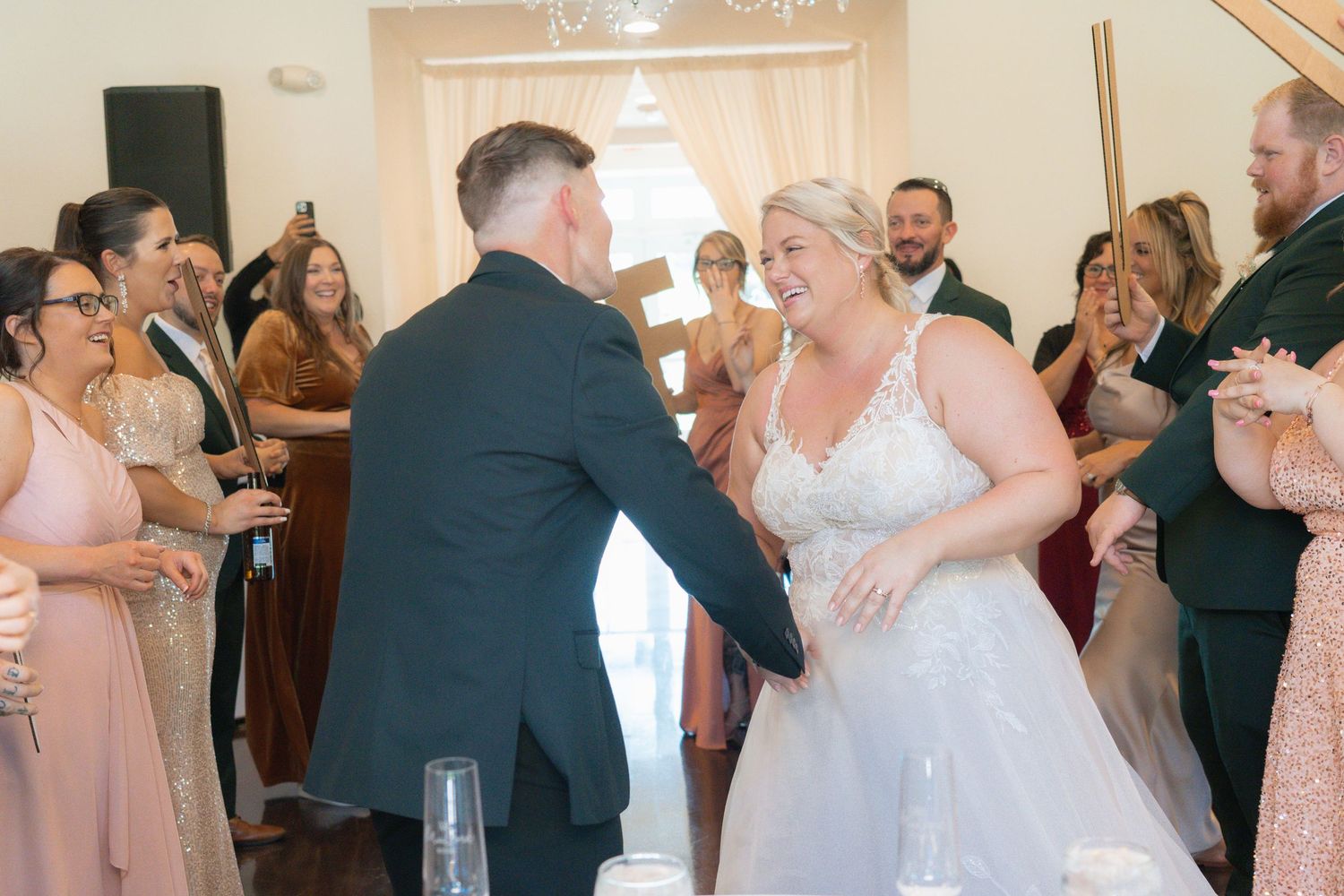Bride and groom share a joyful dance surrounded by wedding guests at their elegant indoor reception.