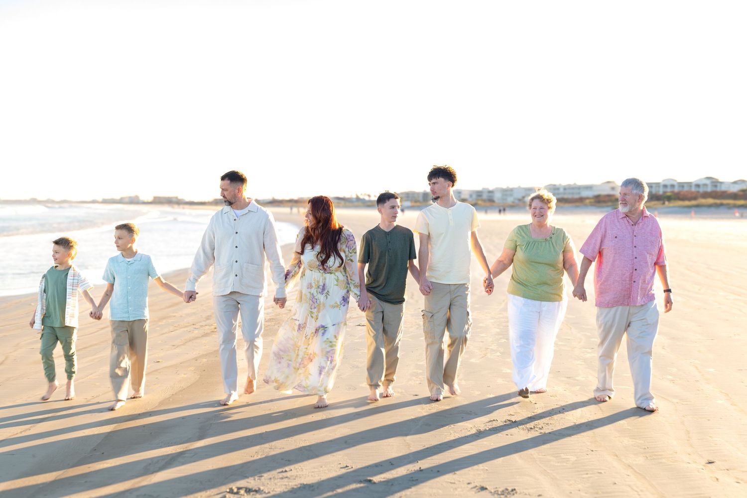 Multi-generational family holding hands walking together on a sunny beach, smiling and enjoying quality time outdoors.
