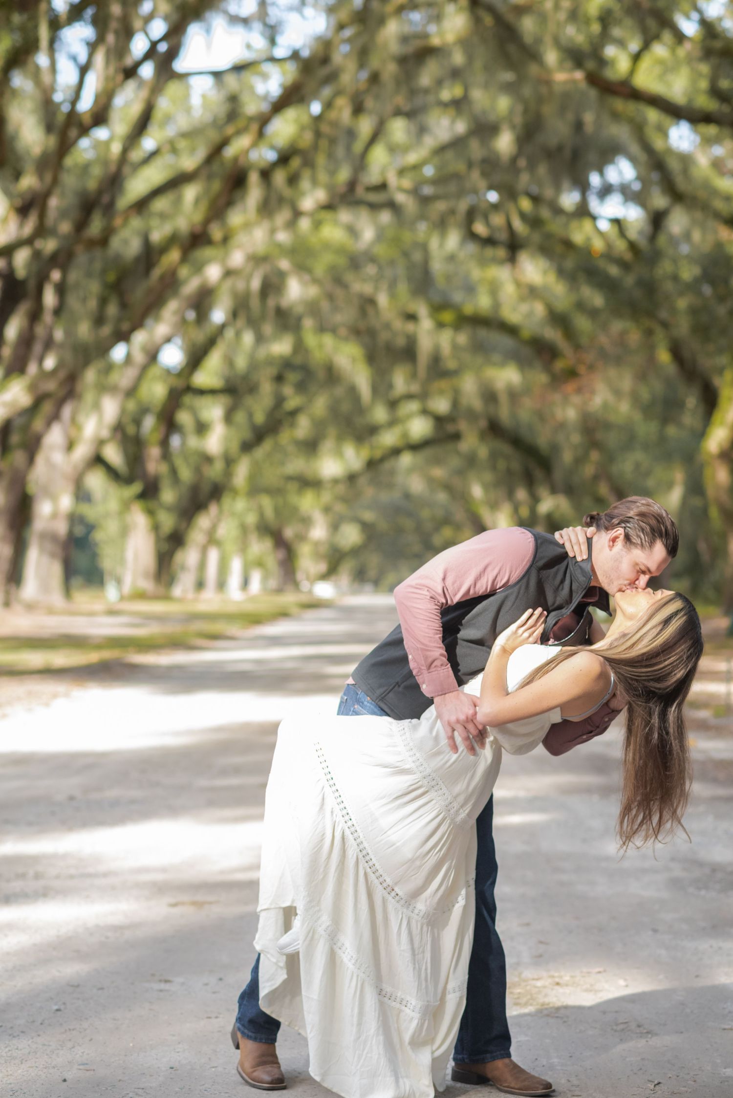 Couple sharing romantic dip kiss on tree-lined path draped with Spanish moss.