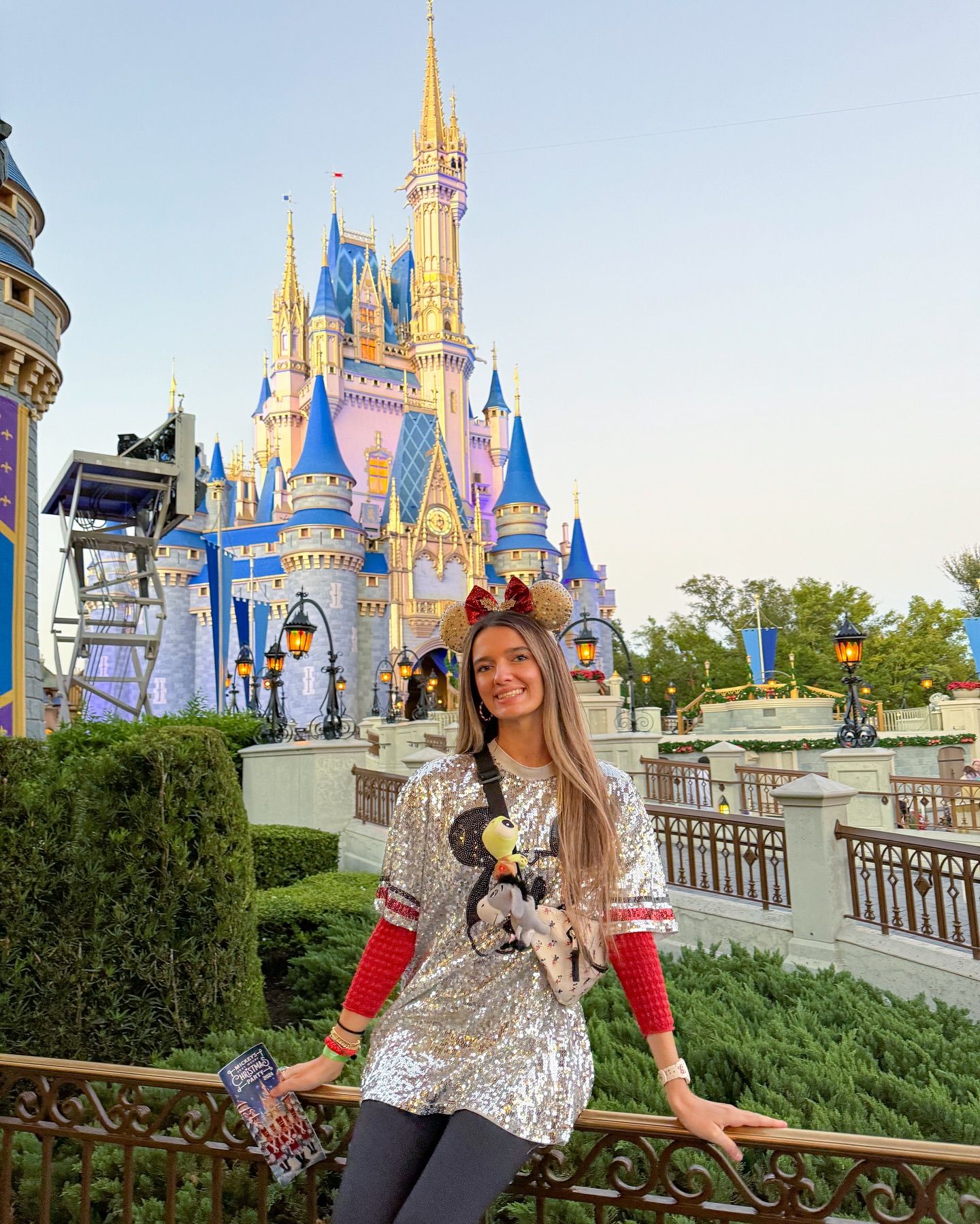 Woman in festive sequin top posing before illuminated Cinderella Castle at Walt Disney World at dusk.