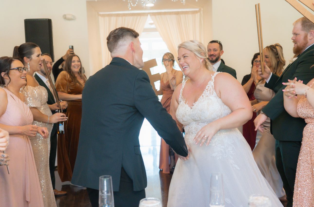 Bride and groom sharing joyful first dance surrounded by celebrating wedding guests.
