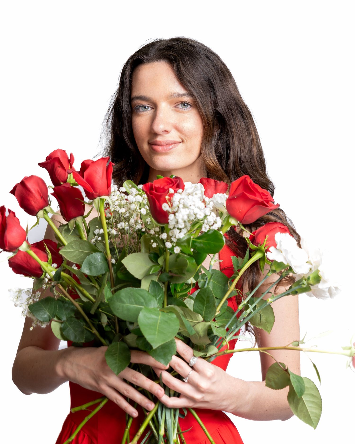 Smiling brunette woman in red dress holding a bouquet of red roses on white background.