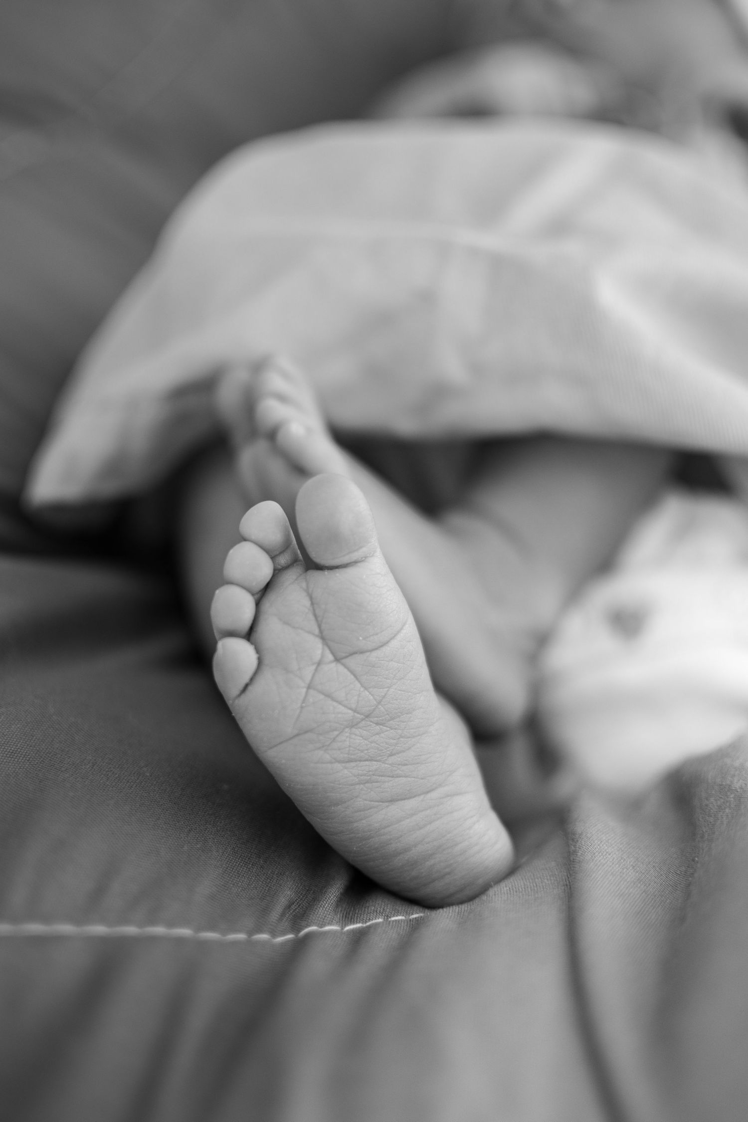 Close-up black and white photo of a newborn baby's tiny foot resting on soft fabric.