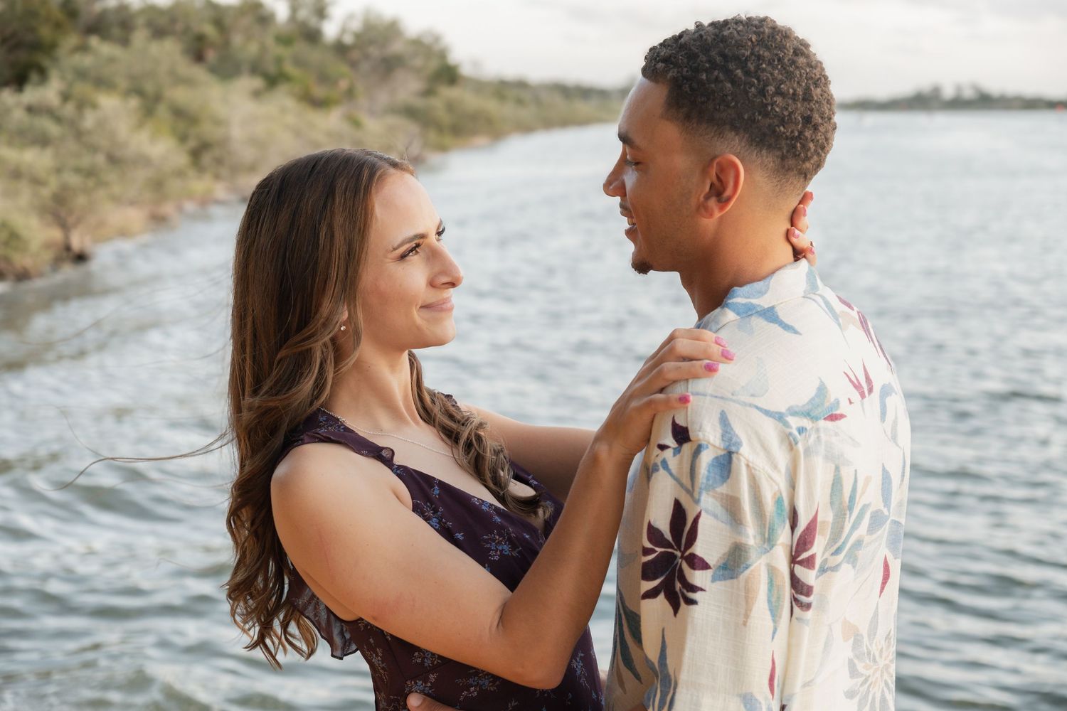Romantic couple sharing a tender moment together near a serene lake with lush greenery in the background.