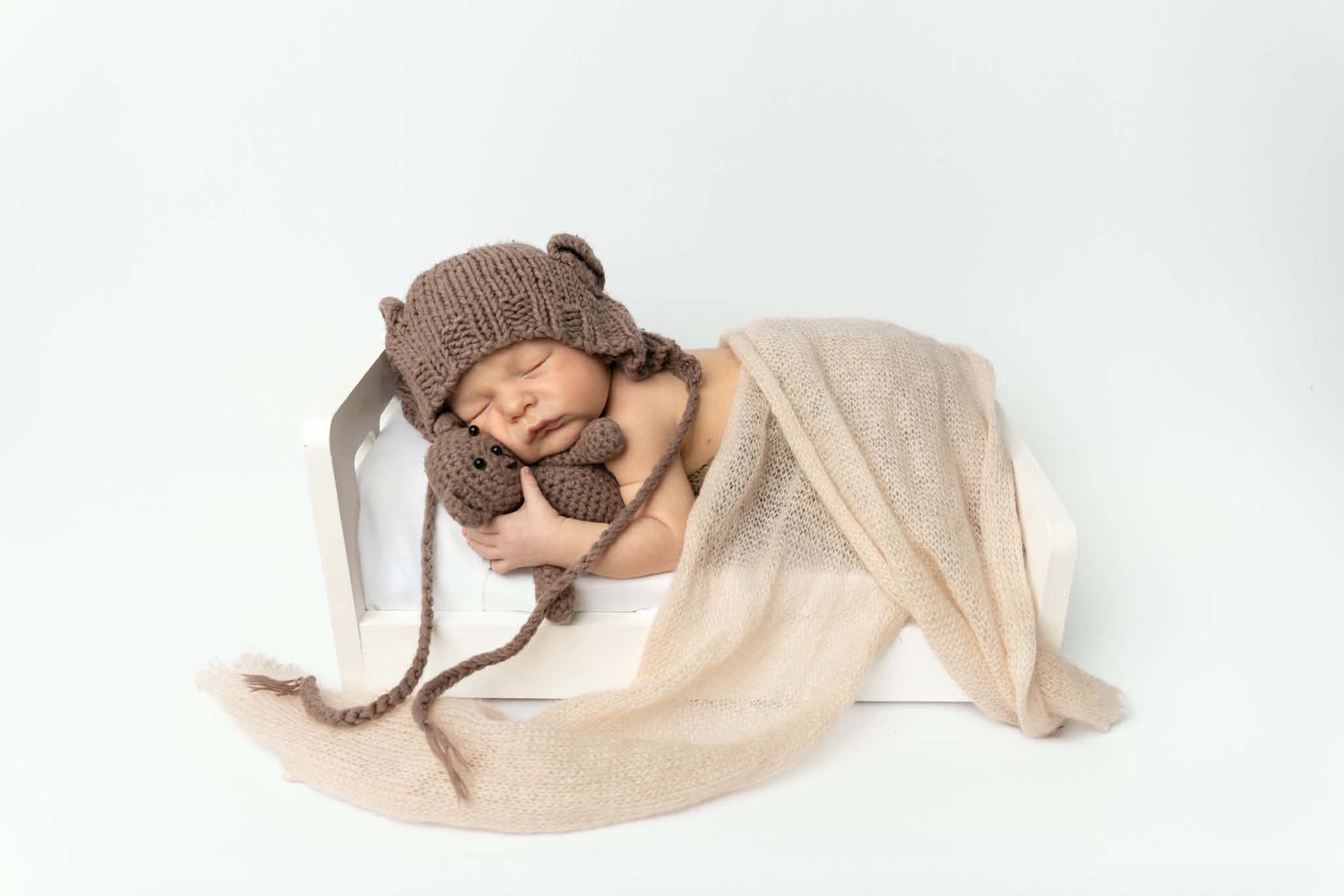 Sleeping newborn in knit bear hat with toy in white box.