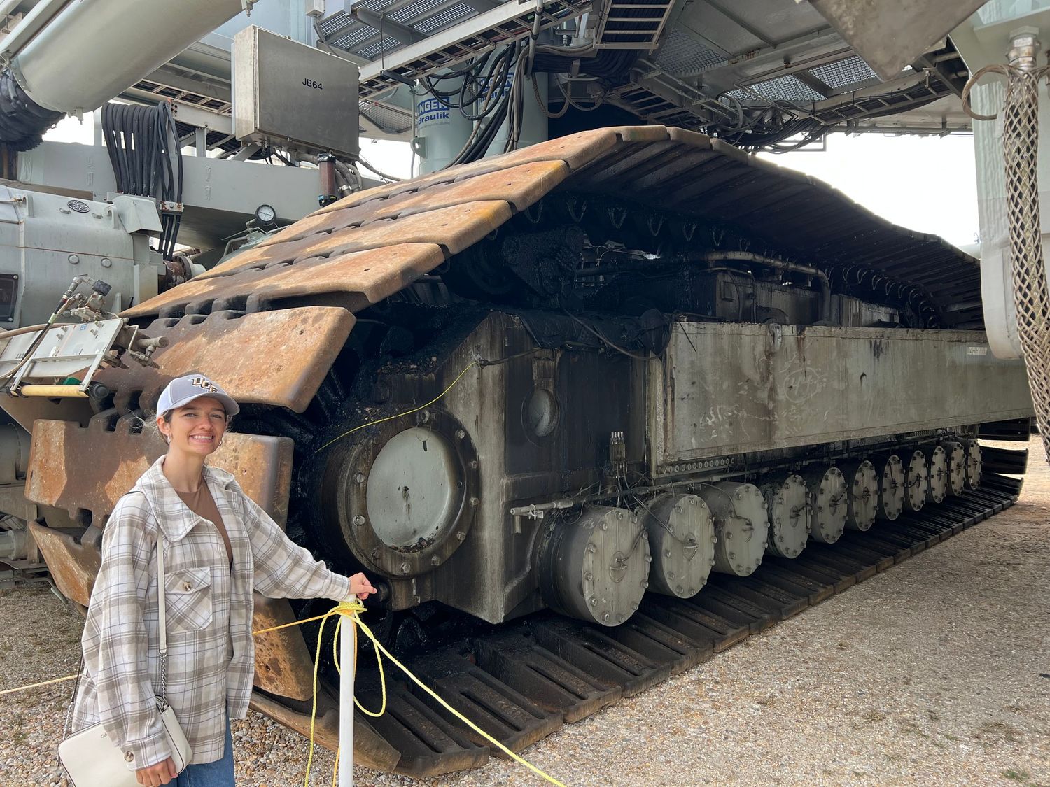 A woman poses beside a large military tank on display outdoors.