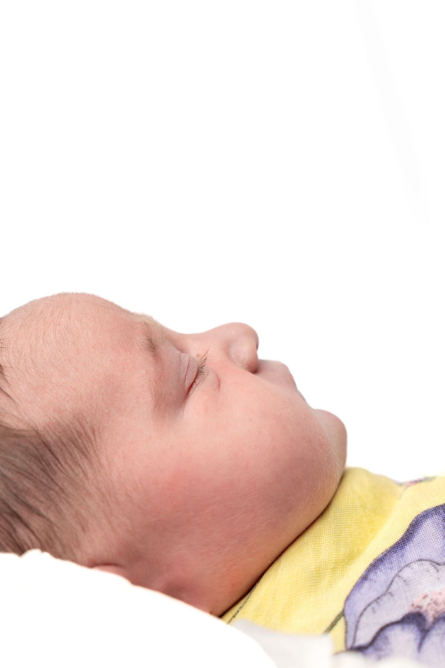 Peaceful newborn baby sleeping on white background, wearing yellow outfit, side profile view.