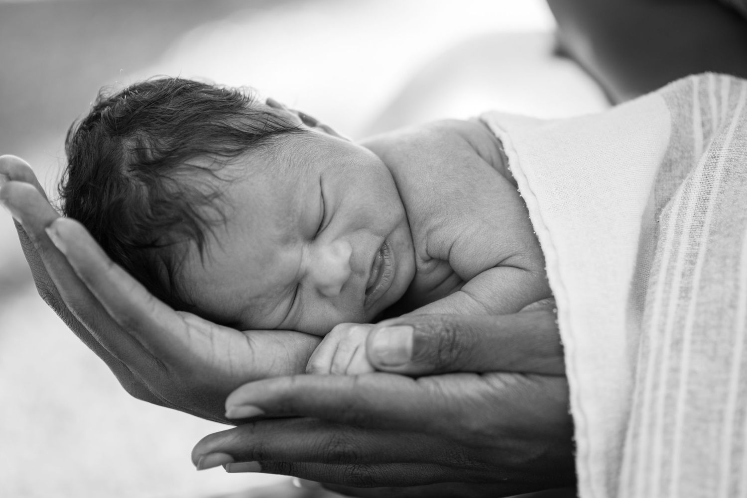 Black and white photo of a sleeping newborn baby cradled gently in an adult's hands.