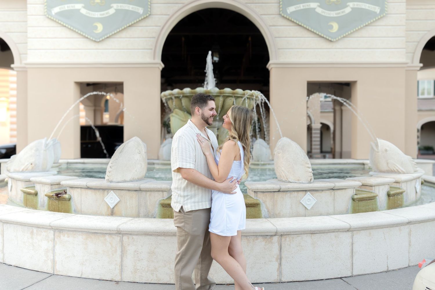 Couple embracing romantically in front of an elegant fountain outdoors.