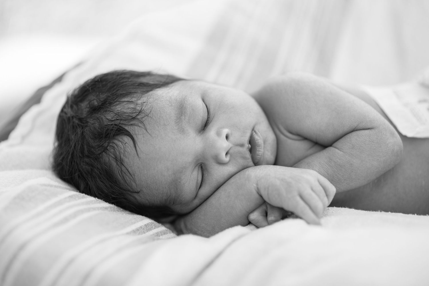 Peaceful newborn baby sleeping curled up on white blanket, black and white photography.