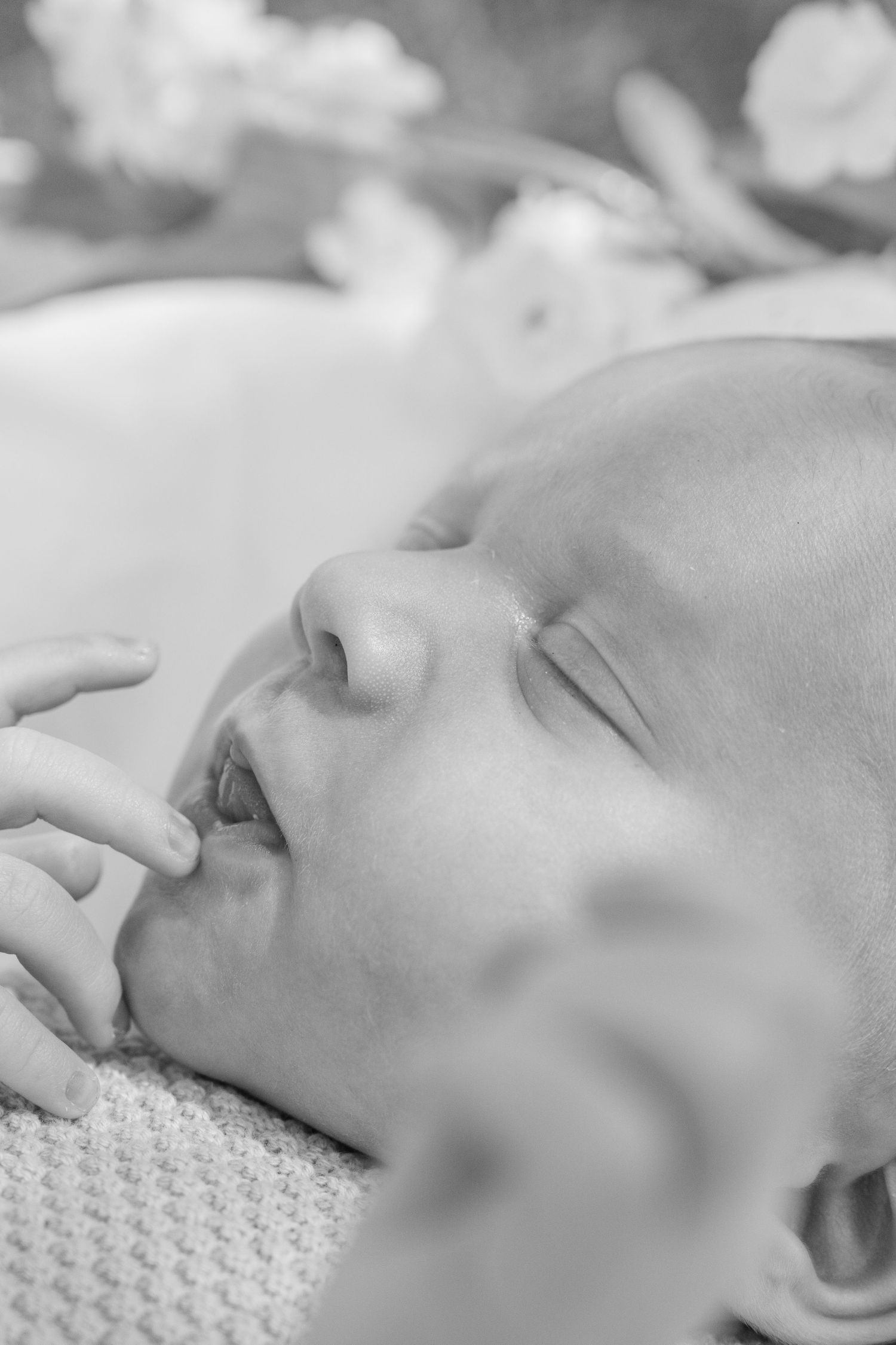 Black and white close-up photo of a peaceful sleeping newborn baby with tiny fingers near face.