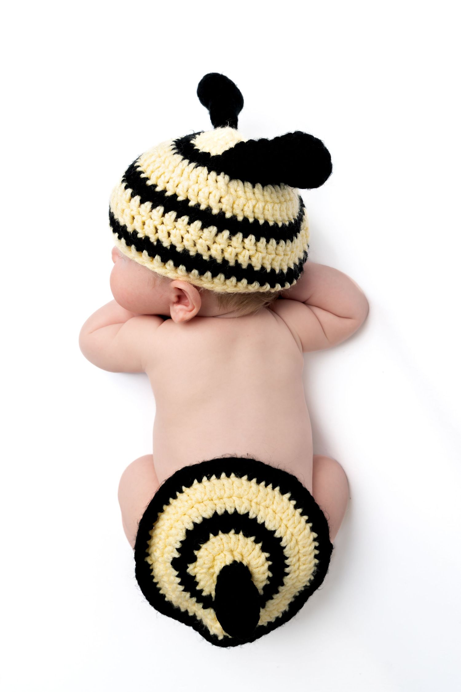 Newborn baby lying face down wearing a crocheted bumblebee hat and diaper cover costume.