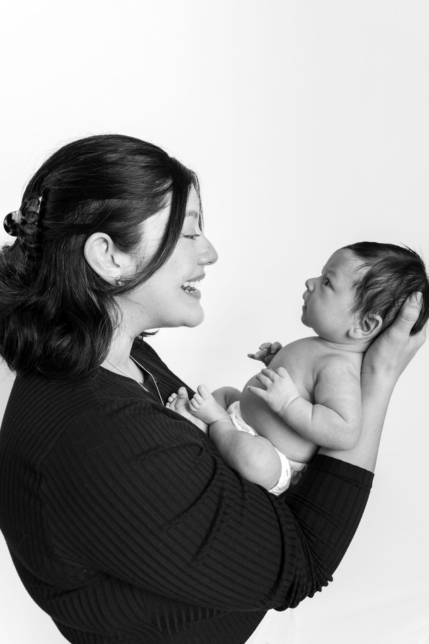 Black and white photo of a smiling mother holding her newborn baby against a white background.