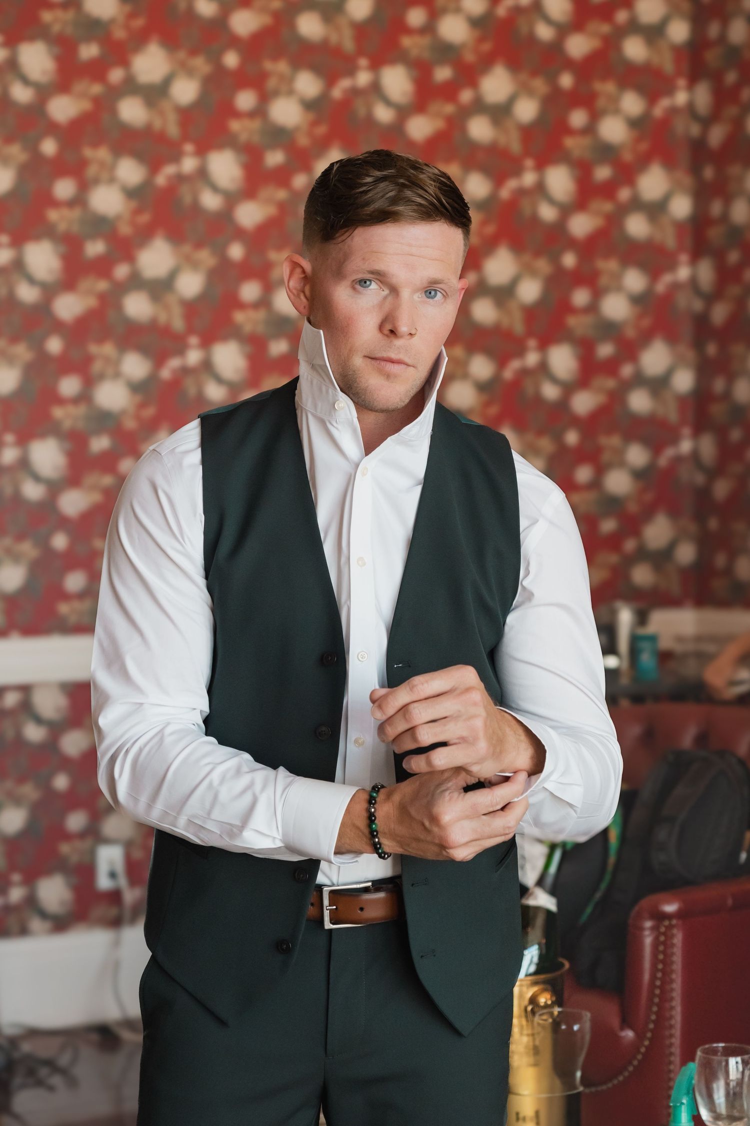 Dapper groom in green vest and white shirt adjusts his cufflinks before the wedding ceremony.
