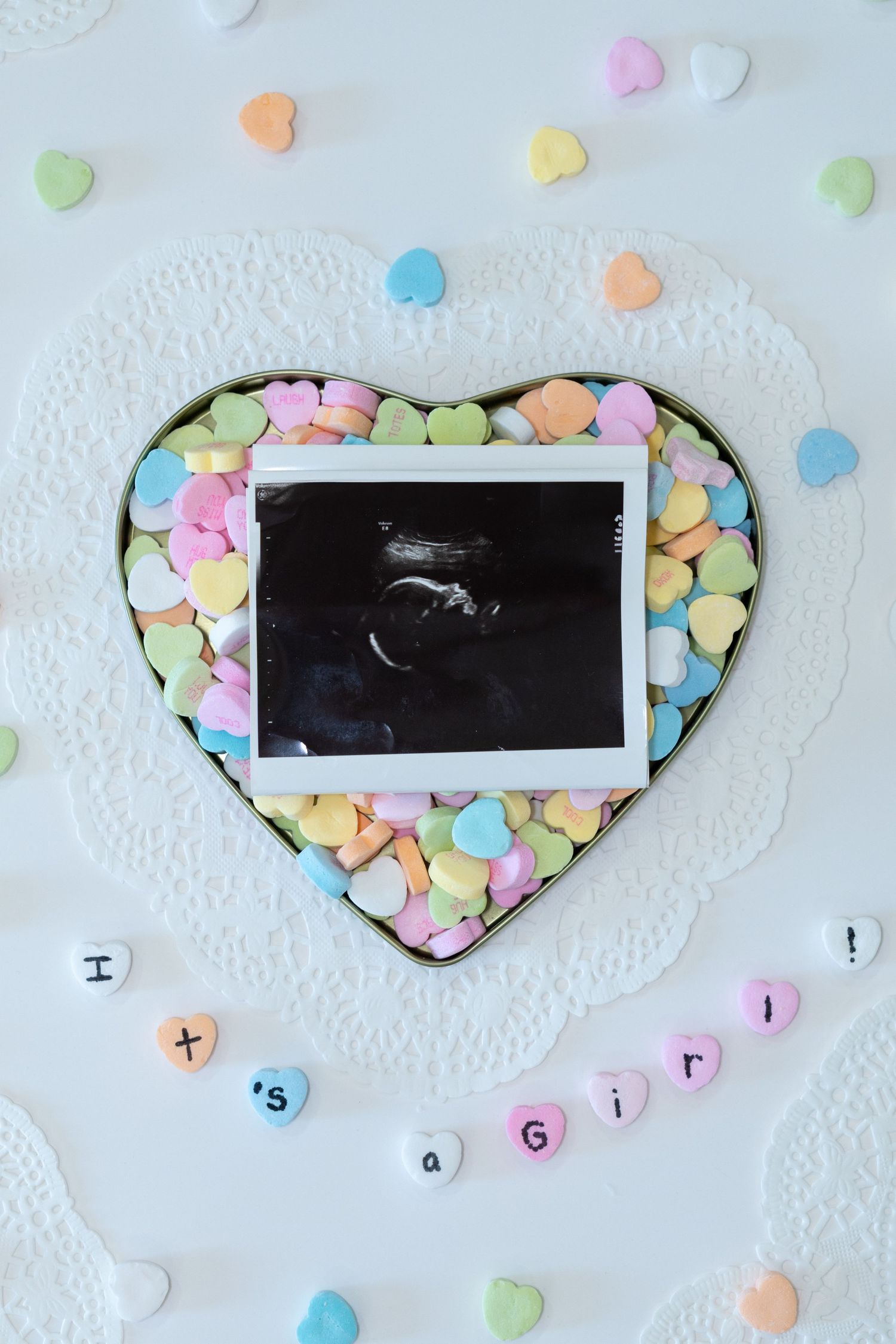 Baby gender reveal with ultrasound photo in heart candy box spelling It's a Girl with pastel conversation hearts.