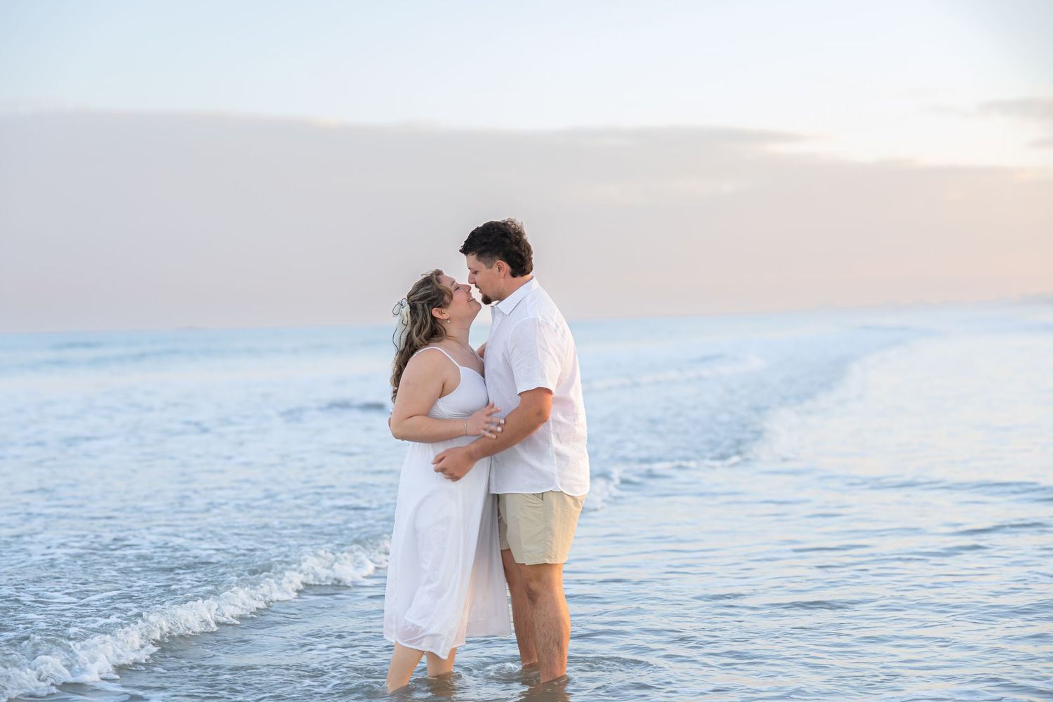 Romantic couple kissing while standing in ocean waves at sunset on the beach.